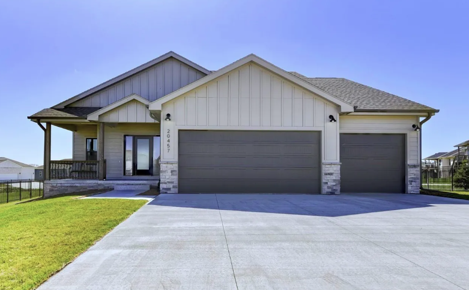 Front view of a modern suburban house with three garage doors, a small front porch, and a well-maintained lawn under a clear blue sky.