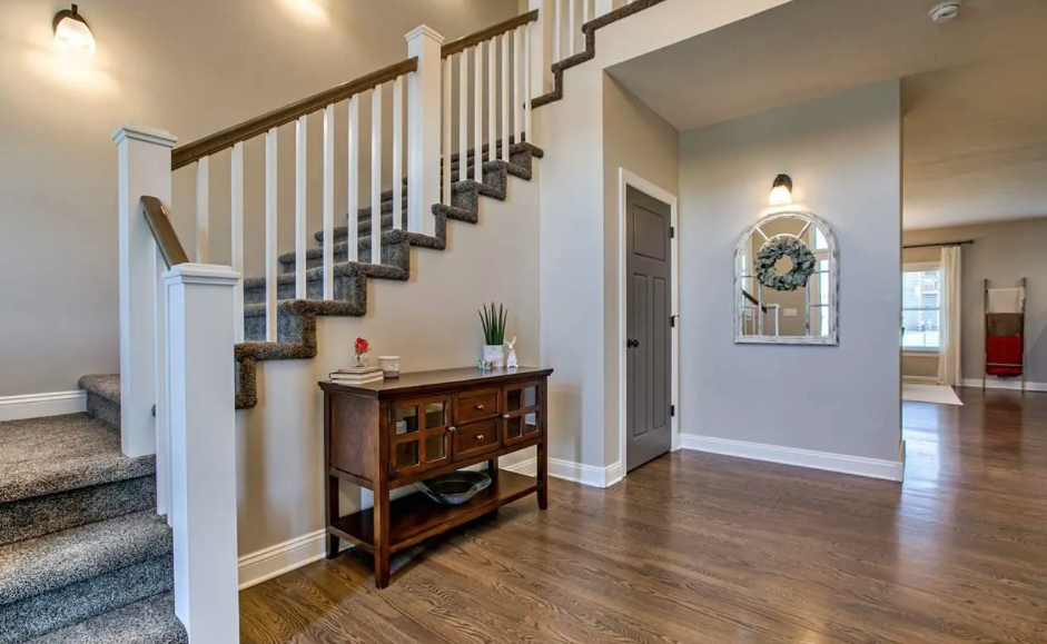 Interior of a home entryway with stairs, a small wooden console table, decor, and a mirror with a wreath hanging on the wall.