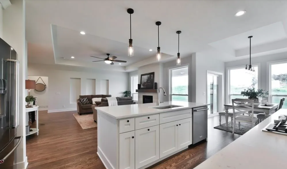 Modern open-concept kitchen and living room with white cabinetry, stainless steel appliances, wood flooring, and large windows.