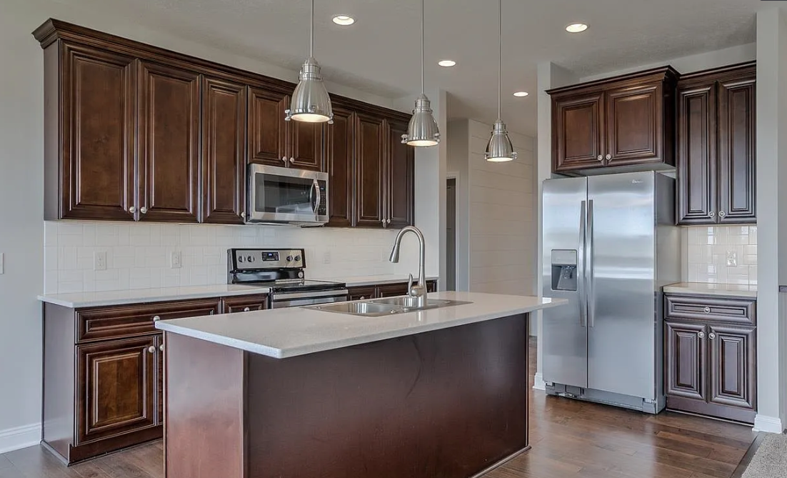 Modern kitchen with dark wood cabinets, stainless steel appliances, a white island with a double sink, pendant lights, and hardwood floors.