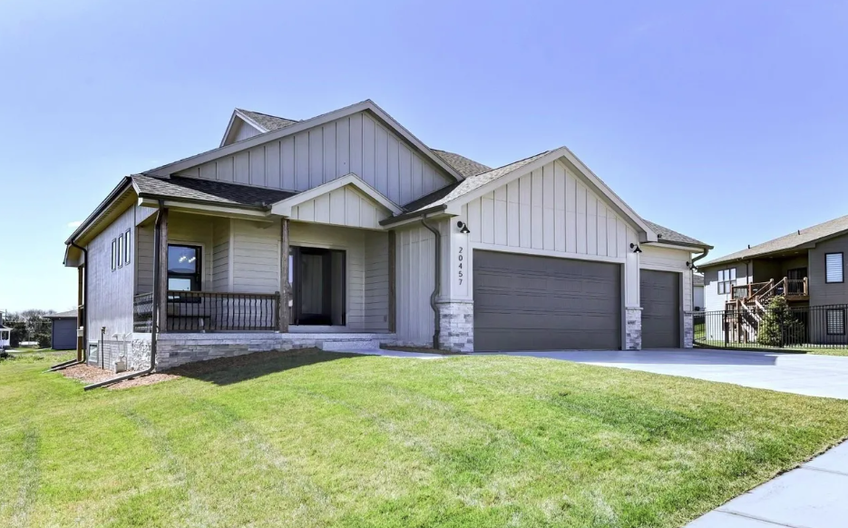 Front view of a modern two-story house with a white exterior, gray garage doors, a small porch, and a green lawn under a clear blue sky.