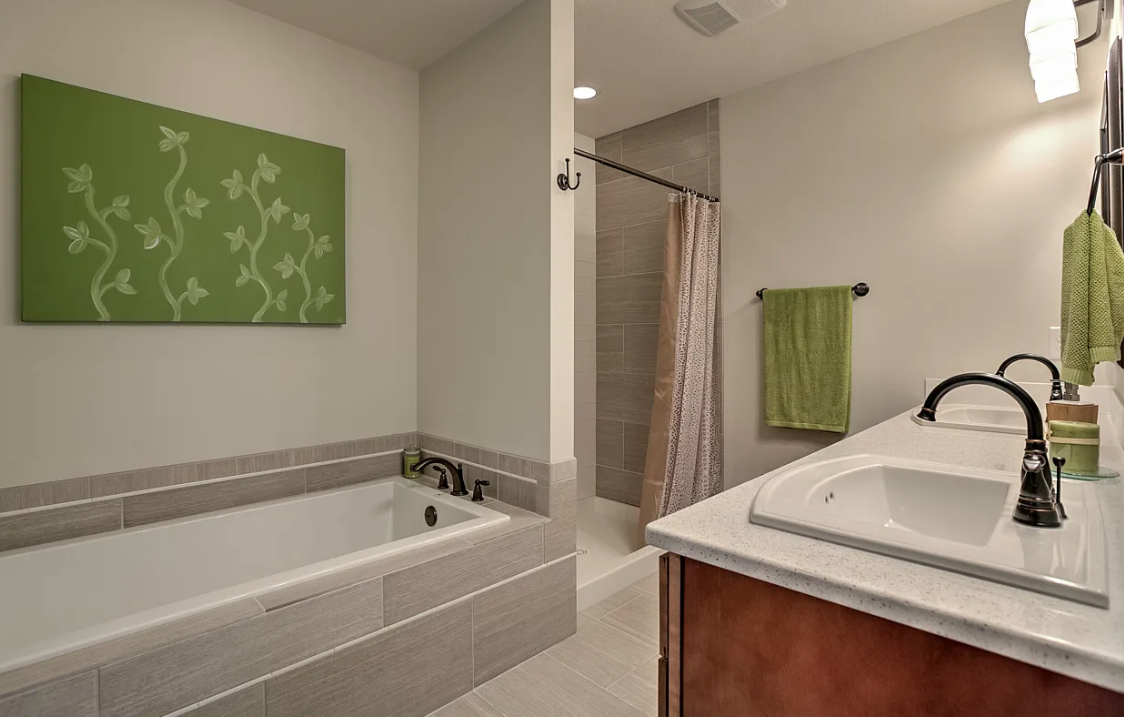 Bathroom with a bathtub, shower area with a curtain, twin sinks with black fixtures, green towels, and a green wall art piece.