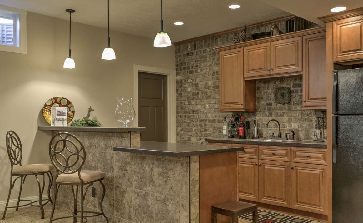 Kitchen with wooden cabinets, a brick accent wall, a black refrigerator, a small sink, and a bar area with two chairs and pendant lights.