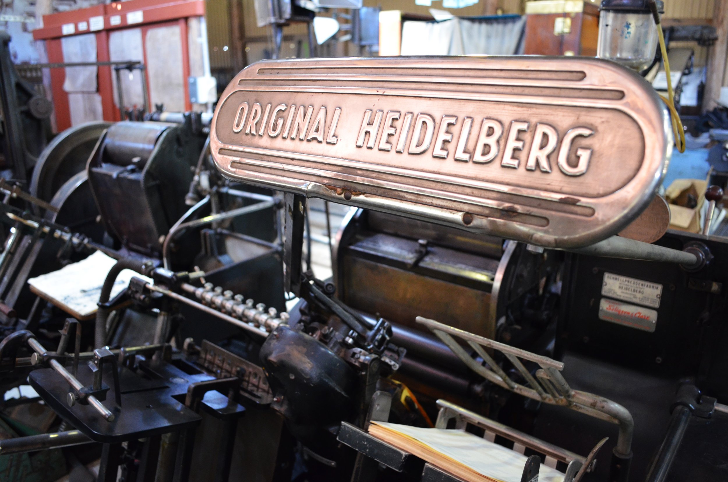 A vintage mechanical printing press with a prominent copper plaque reading 'Original Heidelberg'.