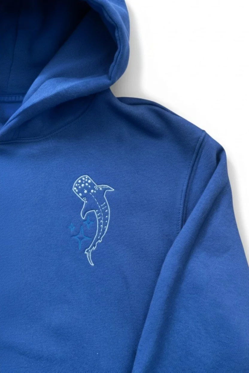 Detailed close up shot of high density thread embroidery showing blue star accents and whale shark texture on navy cotton fabric