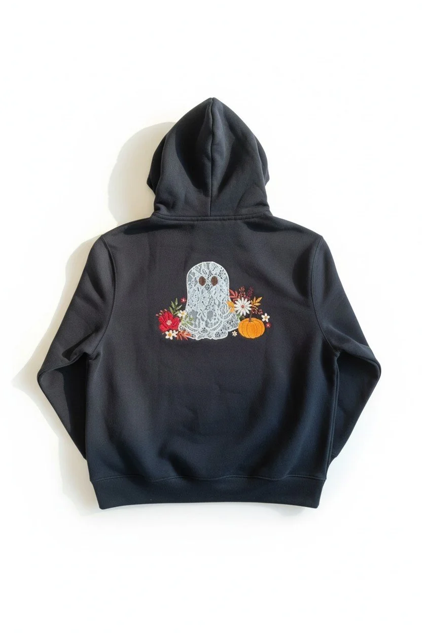 Back of black Halloween hoodie featuring detailed lace-style ghost embroidery with autumn florals and pumpkin accents.