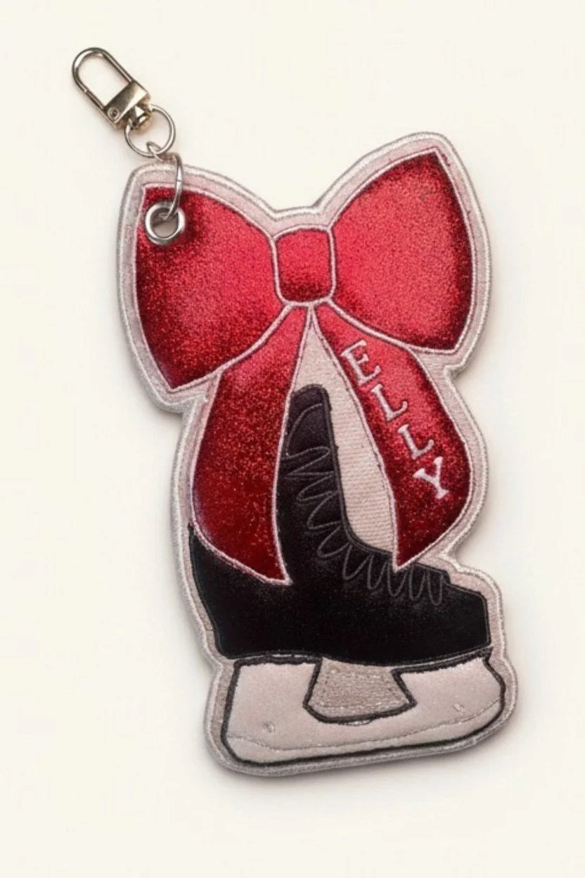 Embroidered hockey skate bow bag charm with pink glitter details and a gold-tone clasp.