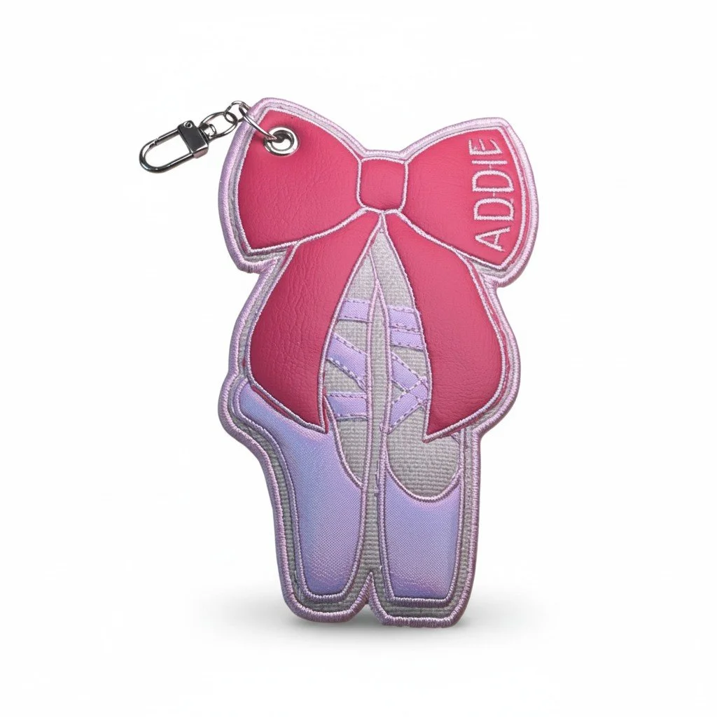 Embroidered ballet pointe shoe bow bag charm with pink details and a gold-tone clasp.