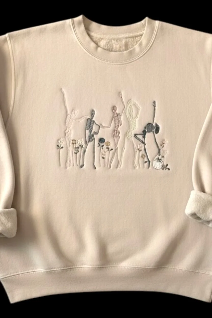 Close-up of detailed embroidery stitching on ivory dancing skeleton Halloween sweatshirt.