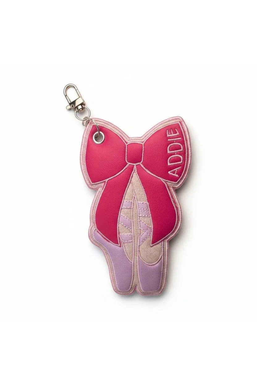 Embroidered ballet pointe shoe bow bag charm with pink details and a gold-tone clasp.