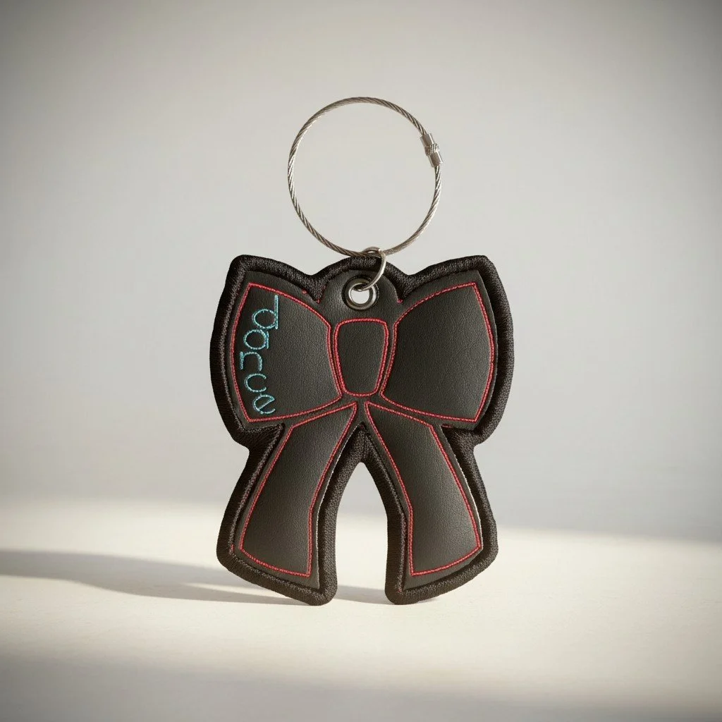 A small, black, bow-shaped keychain with red stitching and blue text that reads "bag love," attached to a metal loop.