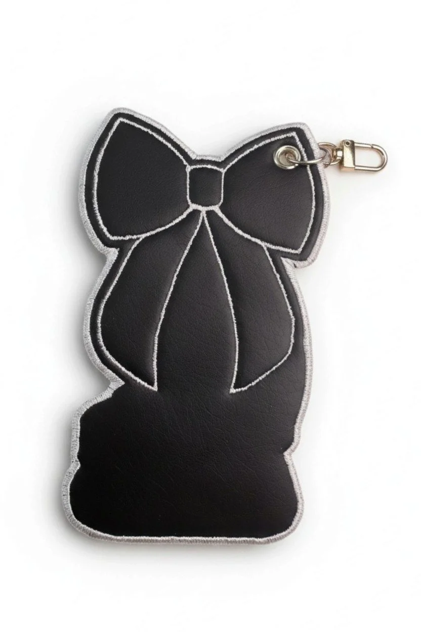 Back detail of embroidered hockey skate bow bag charm with pink glitter details and a gold-tone clasp.