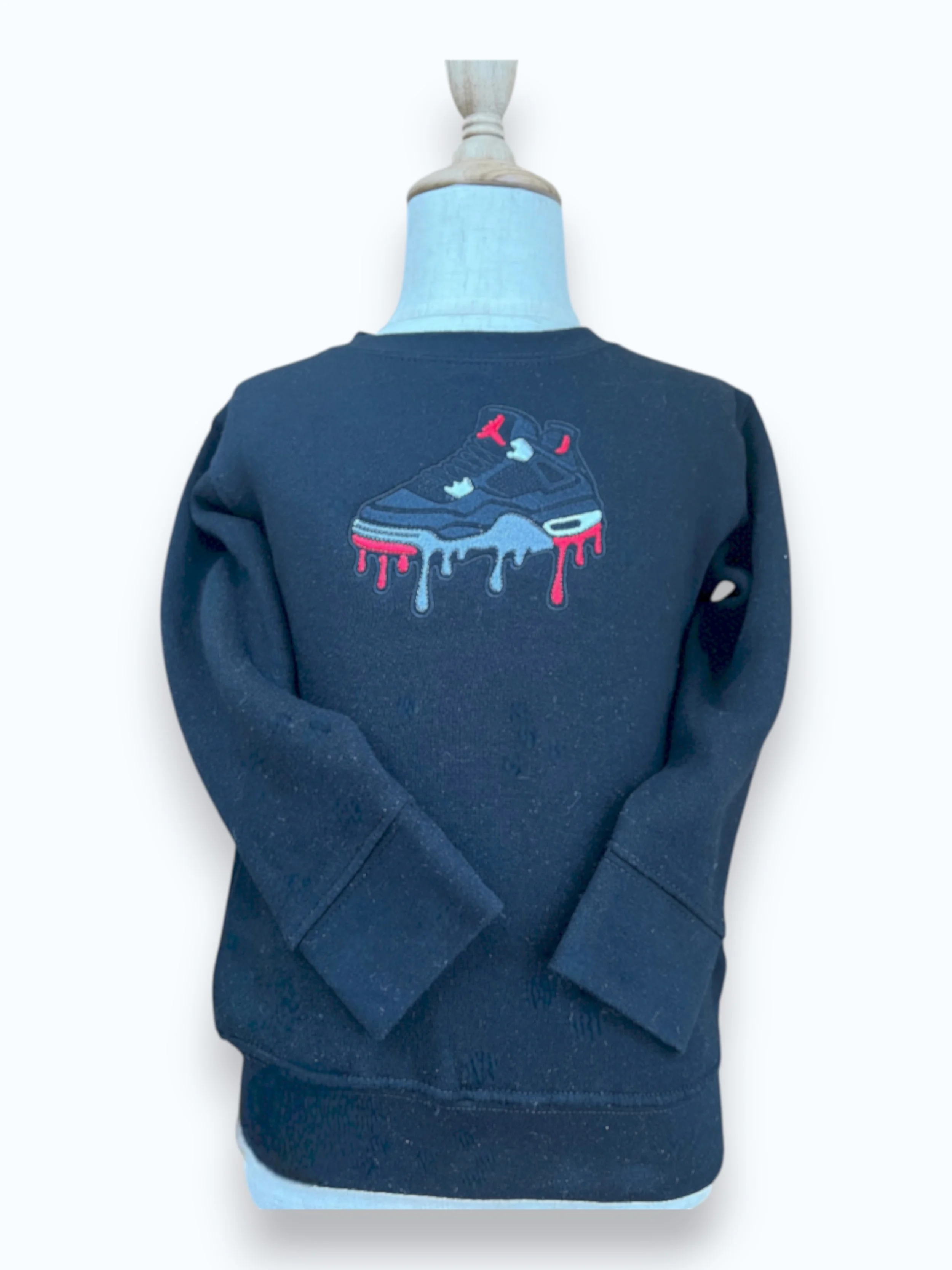 Black sweatshirt with an embroidered design of a sneaker dripping in red, white, and blue on the front.