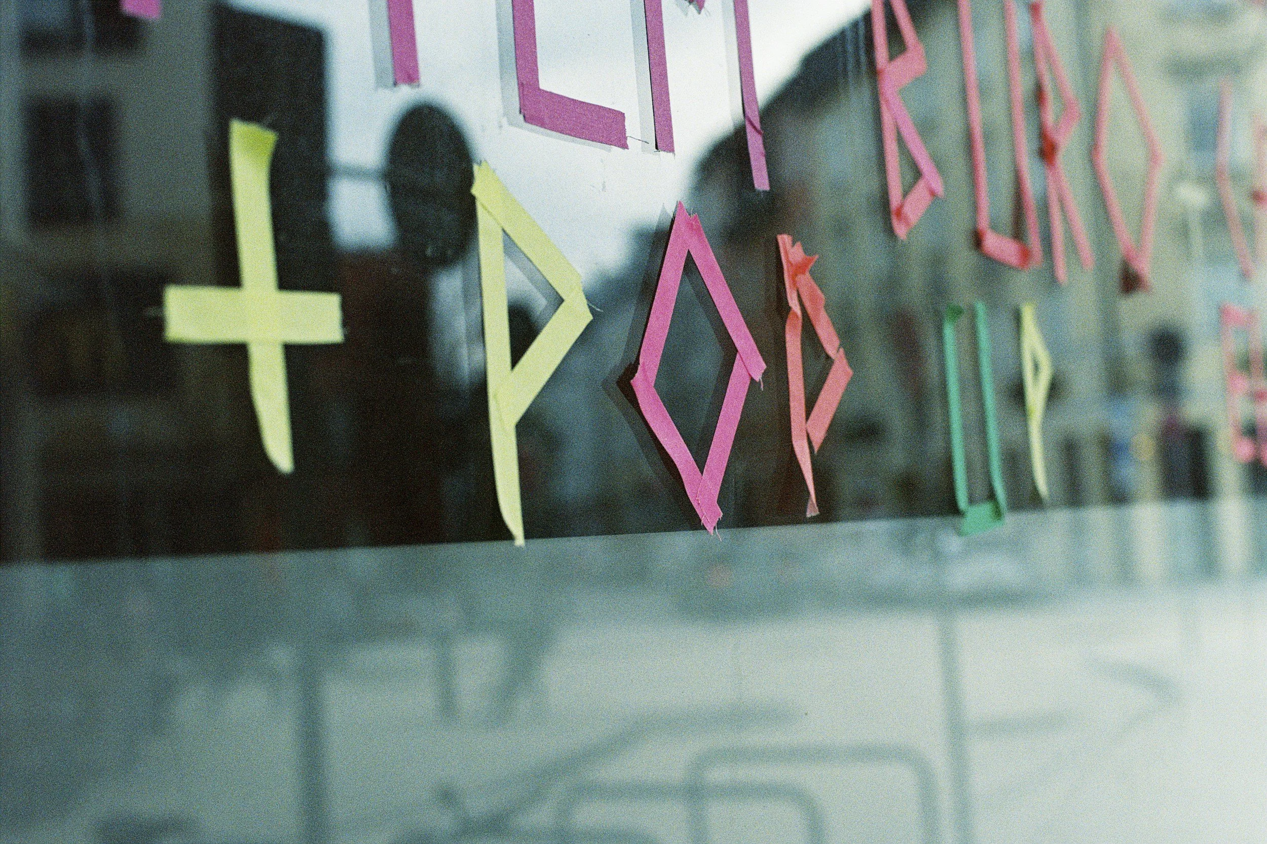 Colorful paper cutouts of geometric shapes like diamonds and X's on a glass surface.