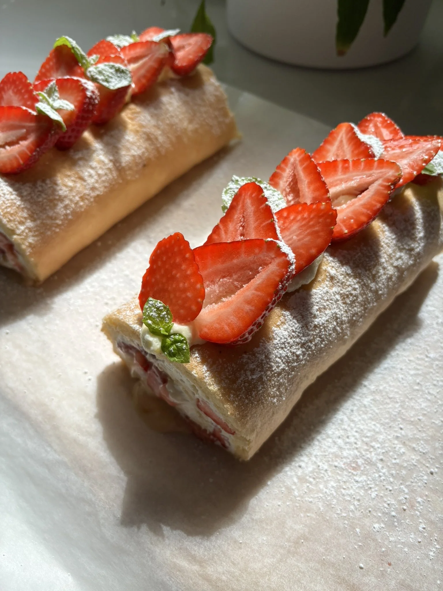 Two strawberry-filled Swiss roll cakes topped with sliced strawberries, powdered sugar, and small green mint leaves.