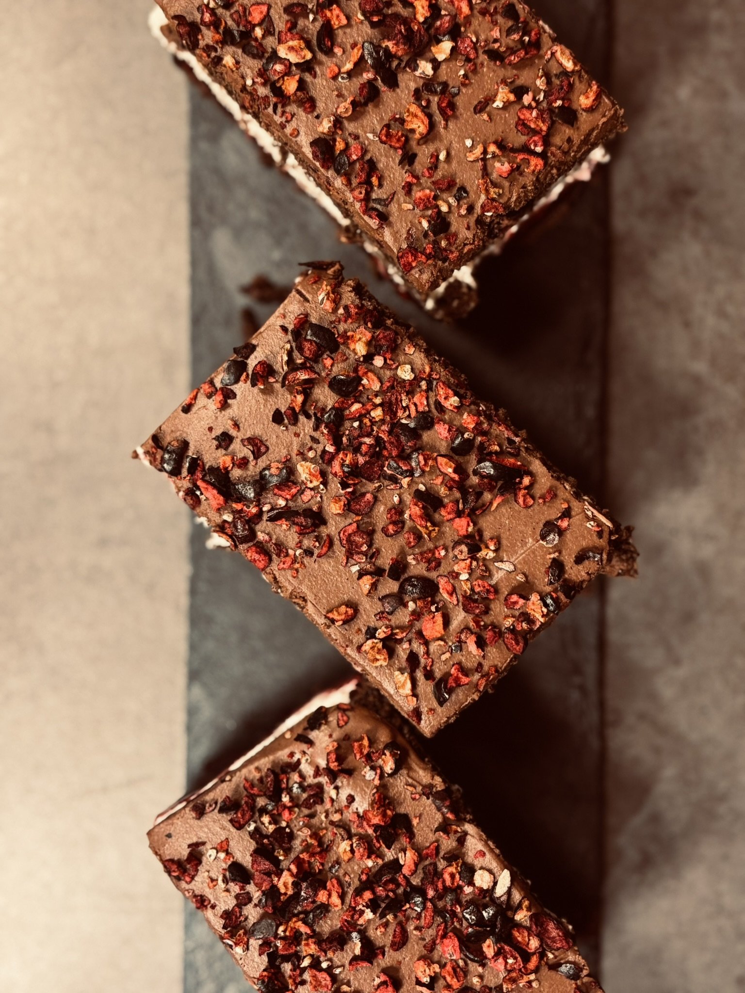 Three pieces of chocolate cake with red and black crushed chili pepper topping arranged on a black rectangular tray.