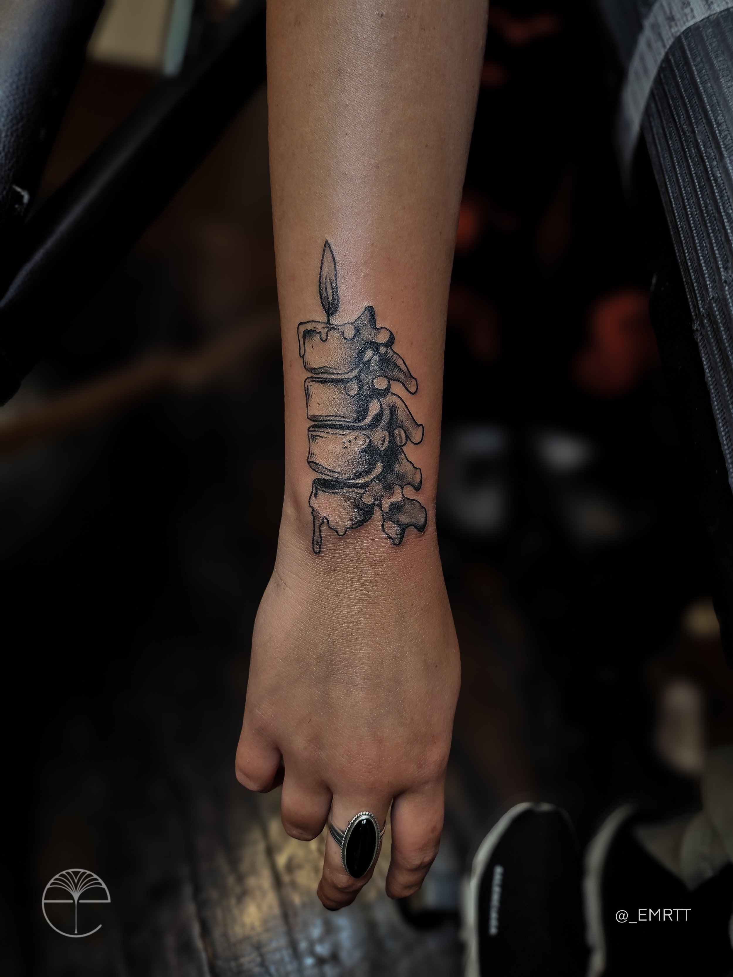 Black tattoo of a melting birthday cake with a lit candle on a person's forearm.