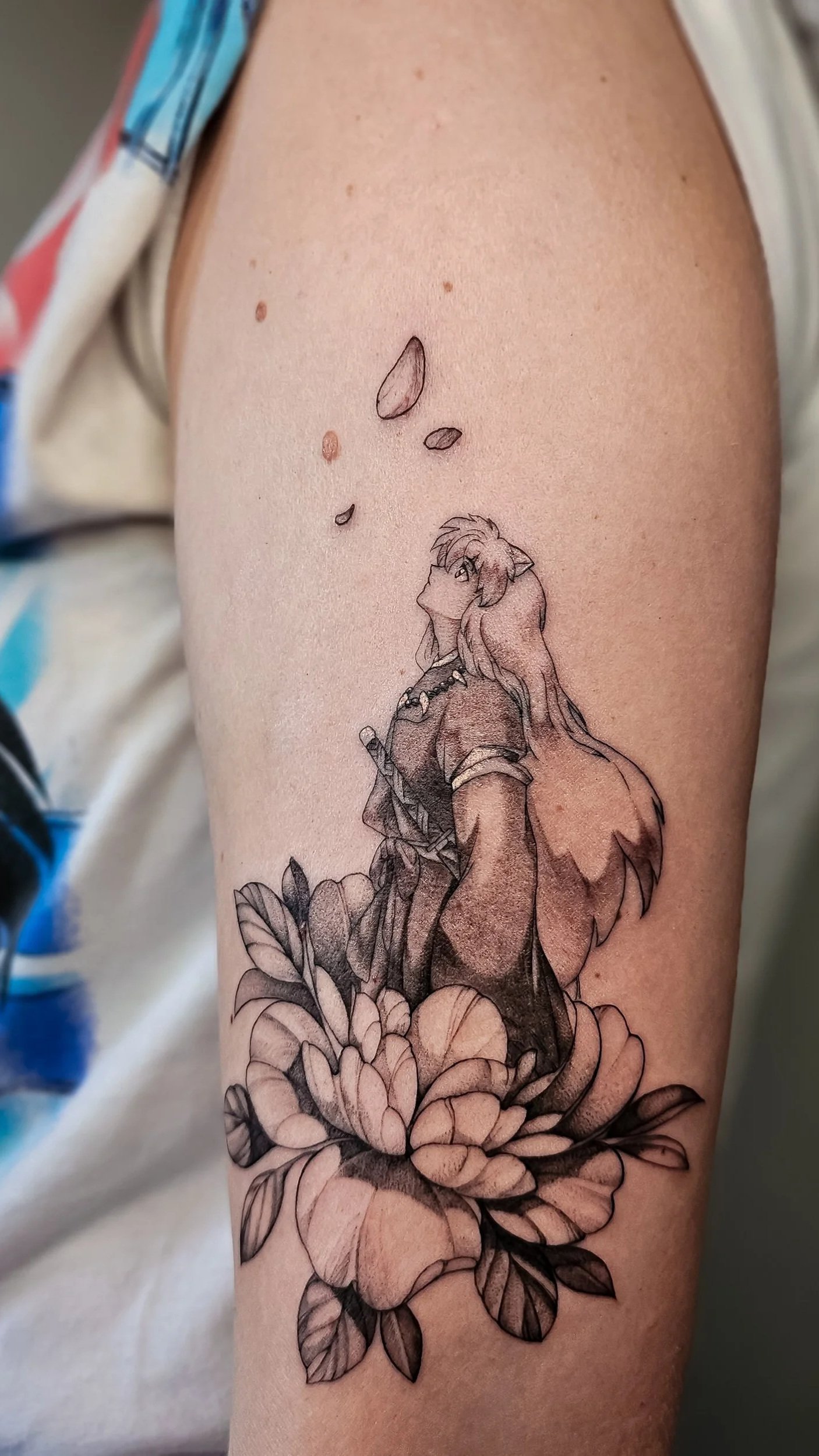 A tattoo of Inuyasha sitting on a flower with petals and leaves, looking upward, with a few flower petals falling above.
