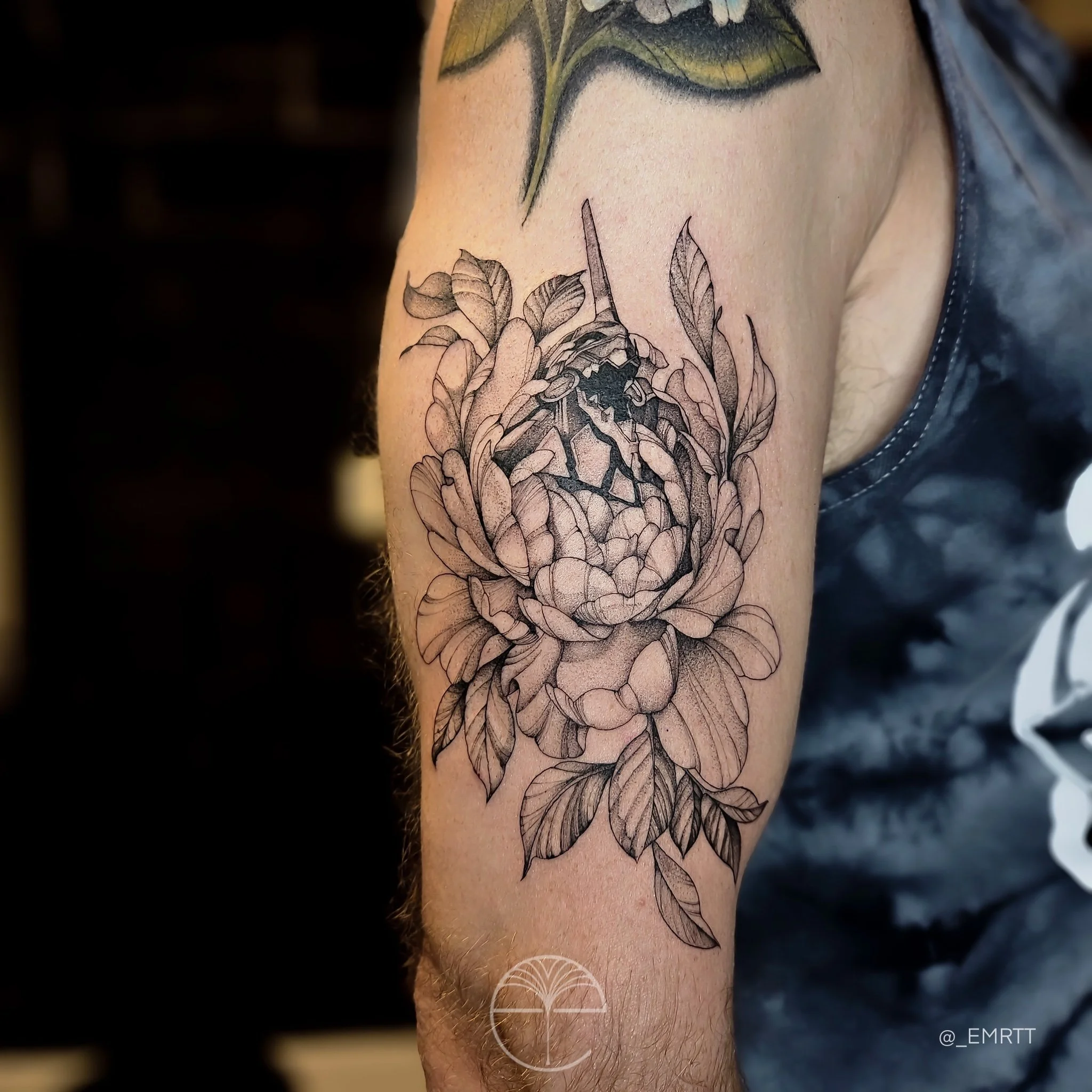A black and gray tattoo of a blooming peony flower with detailed leaves on a person's upper arm.
