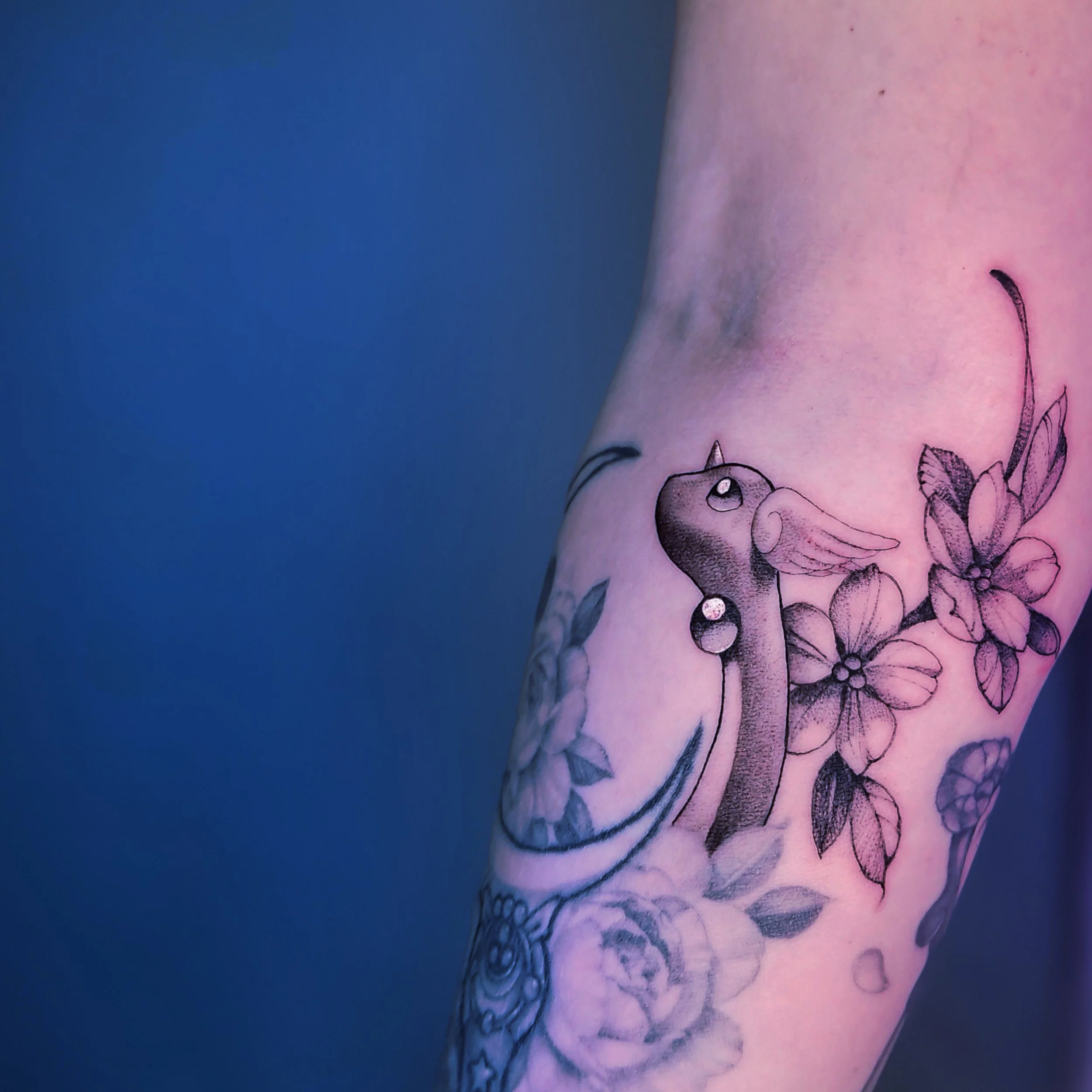 Tattoo of a unicorn with wings and a horn, surrounded by cherry blossoms on a person's arm.