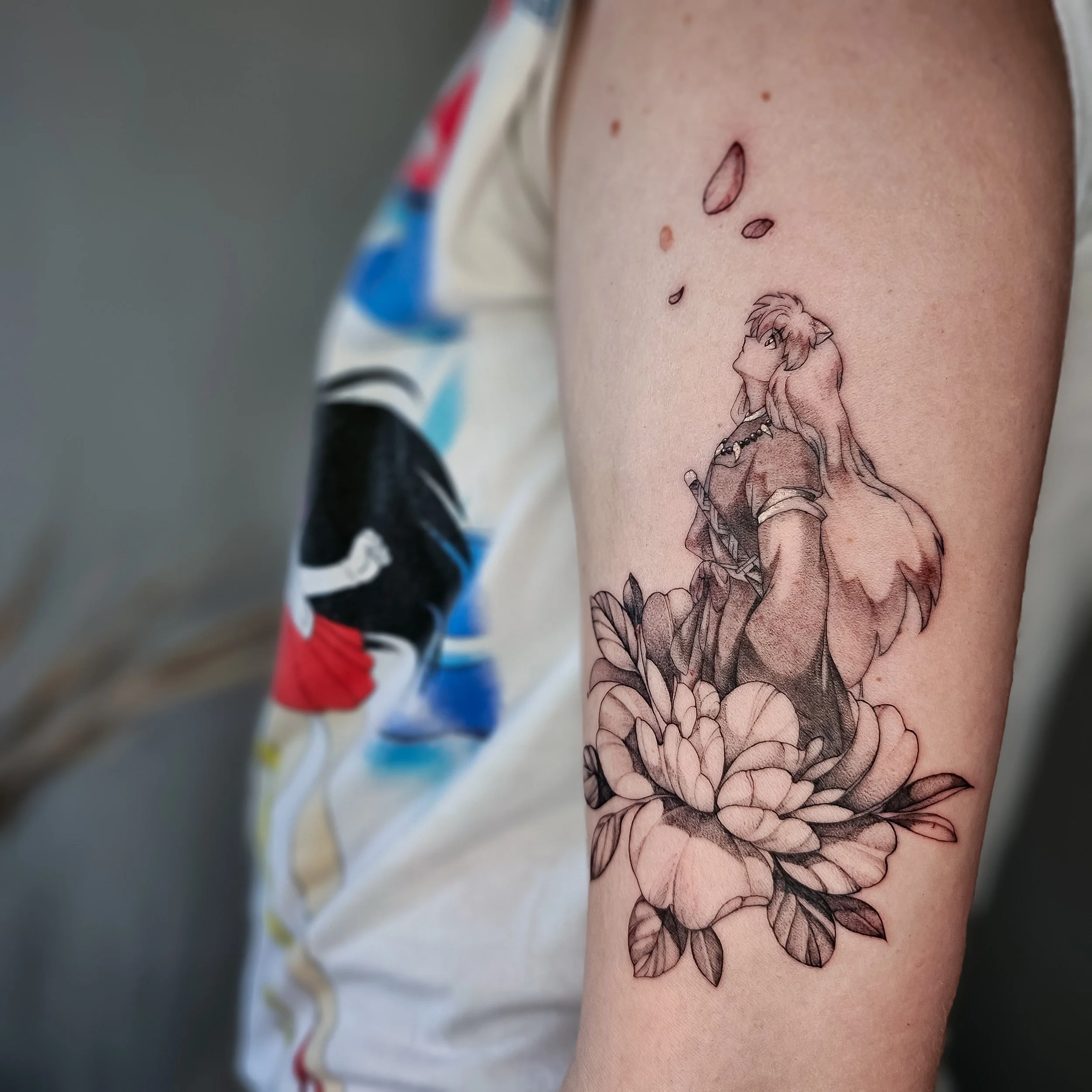 Tattoo of an anime-style character with long hair, standing among large flowers on the person's upper arm.