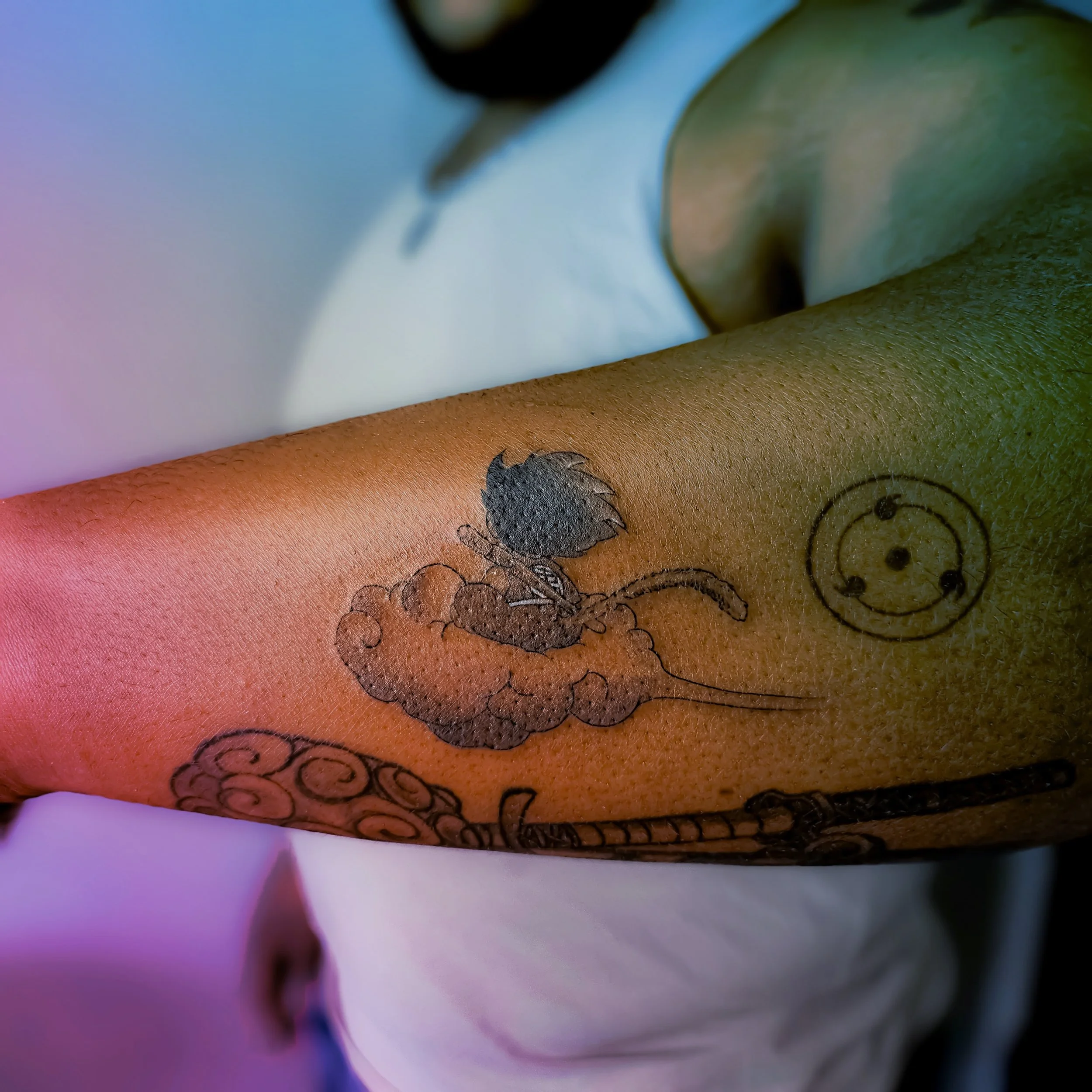 Tattoo of Goku riding Numbus, with a Triple Tomoe Sharingan symbol on a person's forearm.