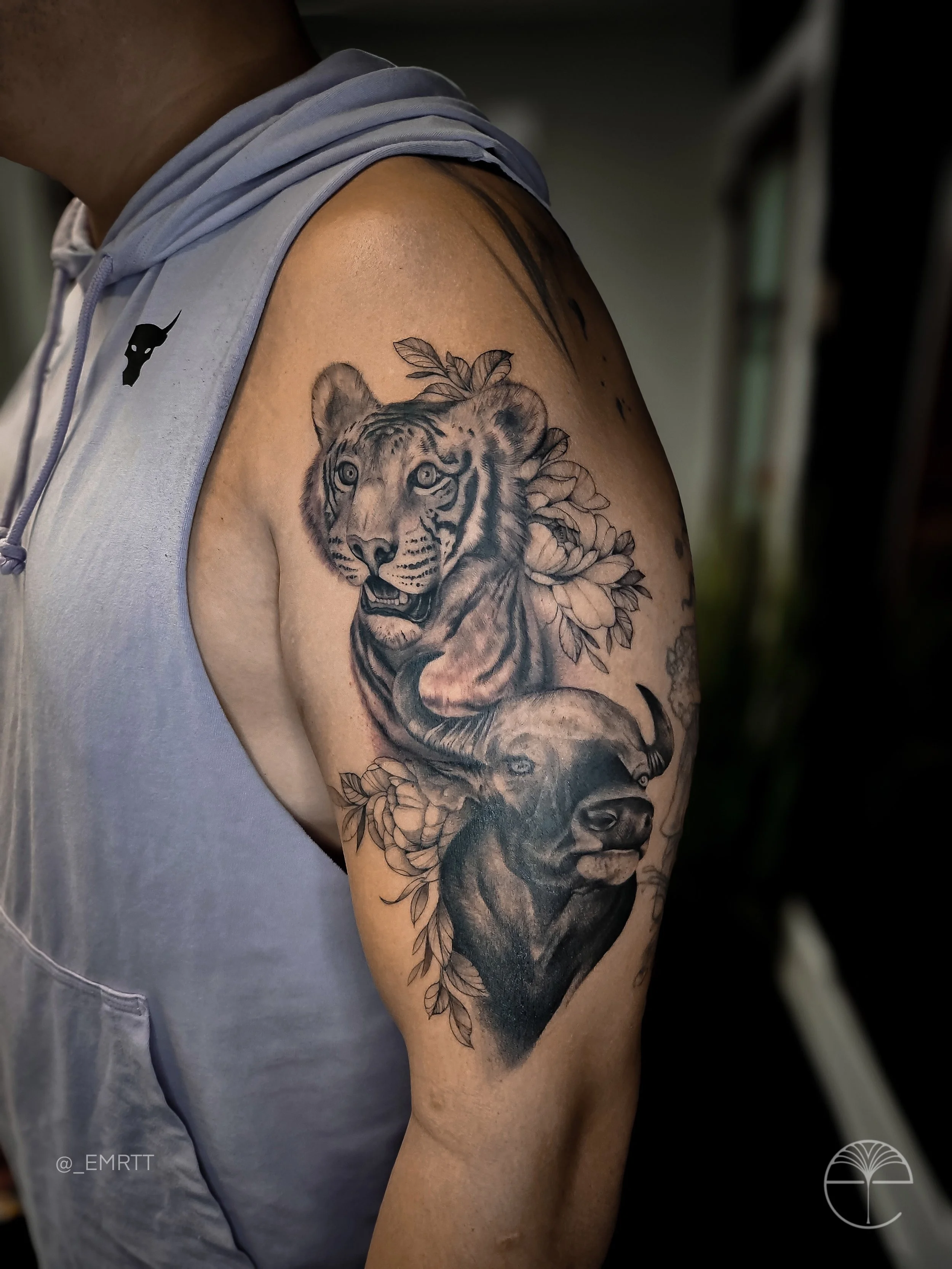 Tattoo of a tiger and a dog on the upper arm with leaves and flowers around them.