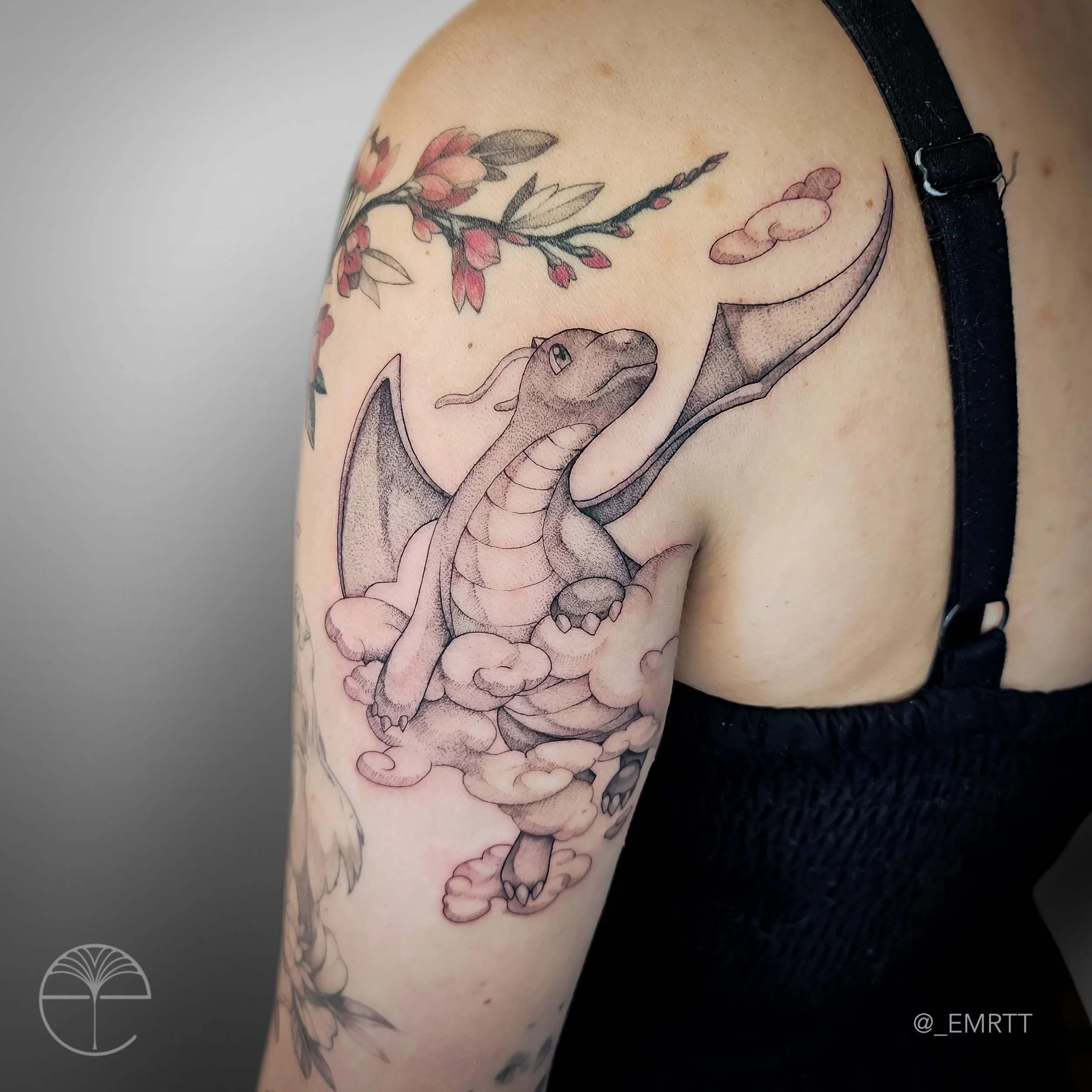 Tattoo of a baby dragon with wings, sitting on clouds, with cherry blossom branches above.