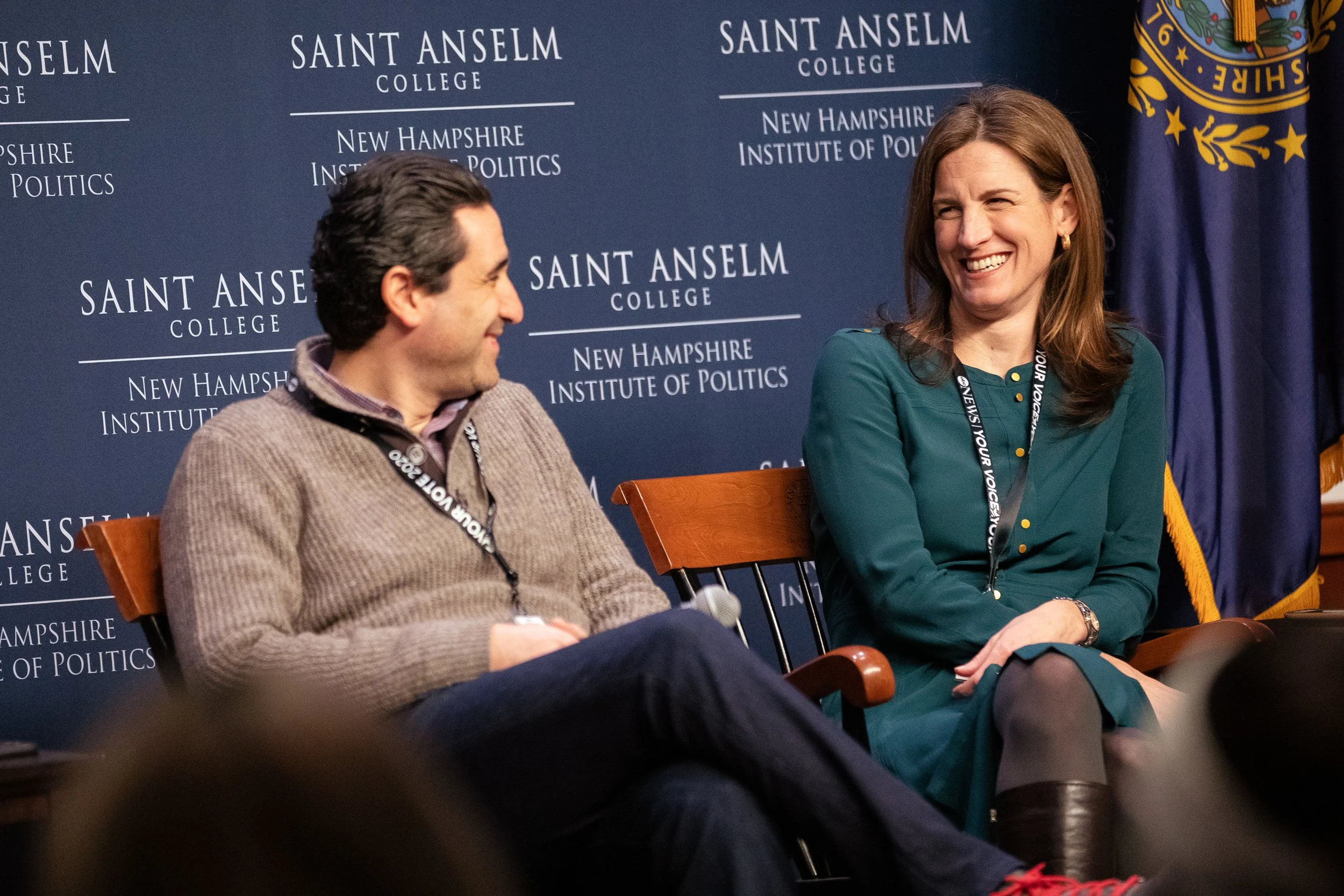 Two people sitting on stage at Saint Anselm College, engaging in a conversation, at the New Hampshire Institute of Politics.