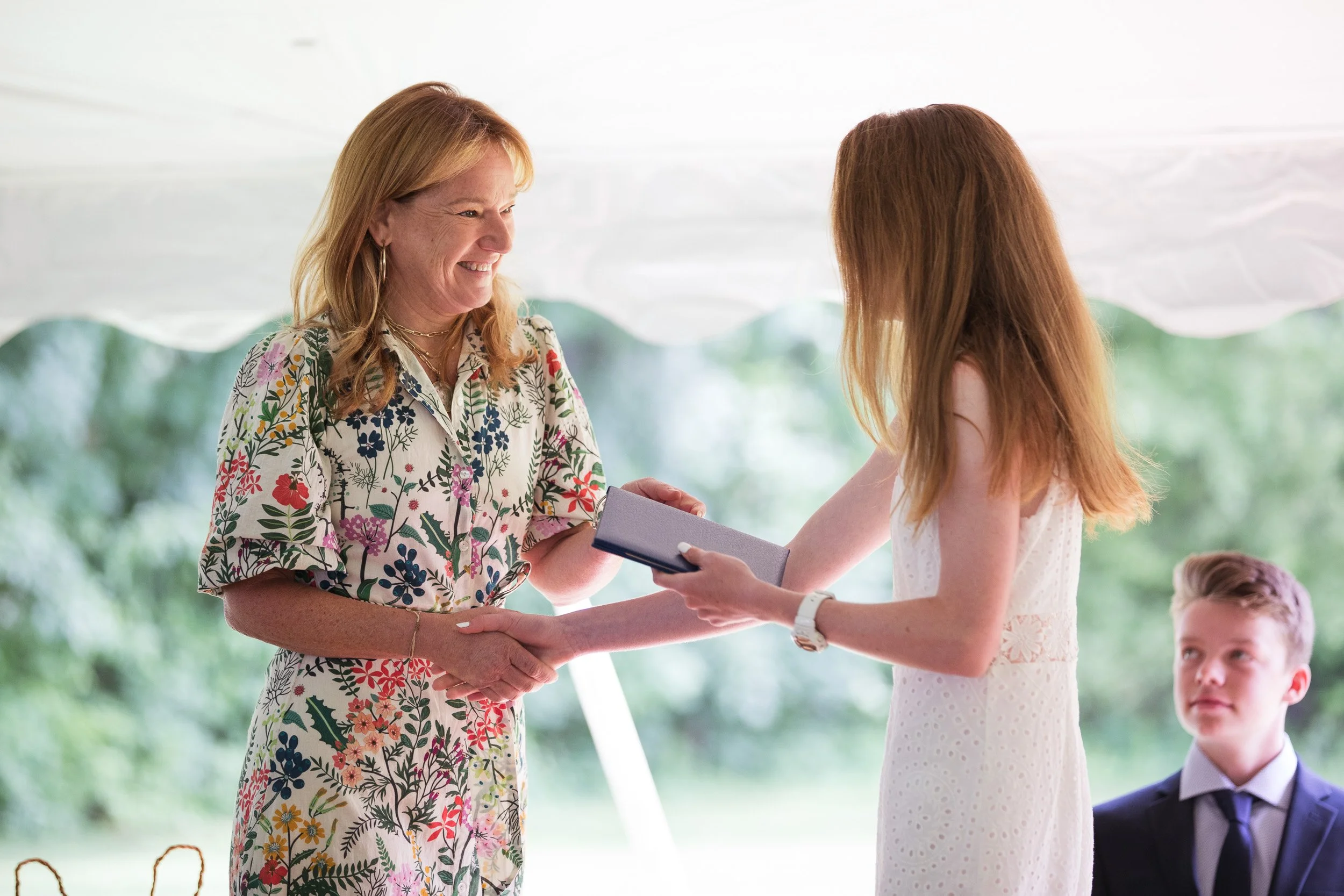 Middle school student receiving diploma at outdoor graduation ceremony.
