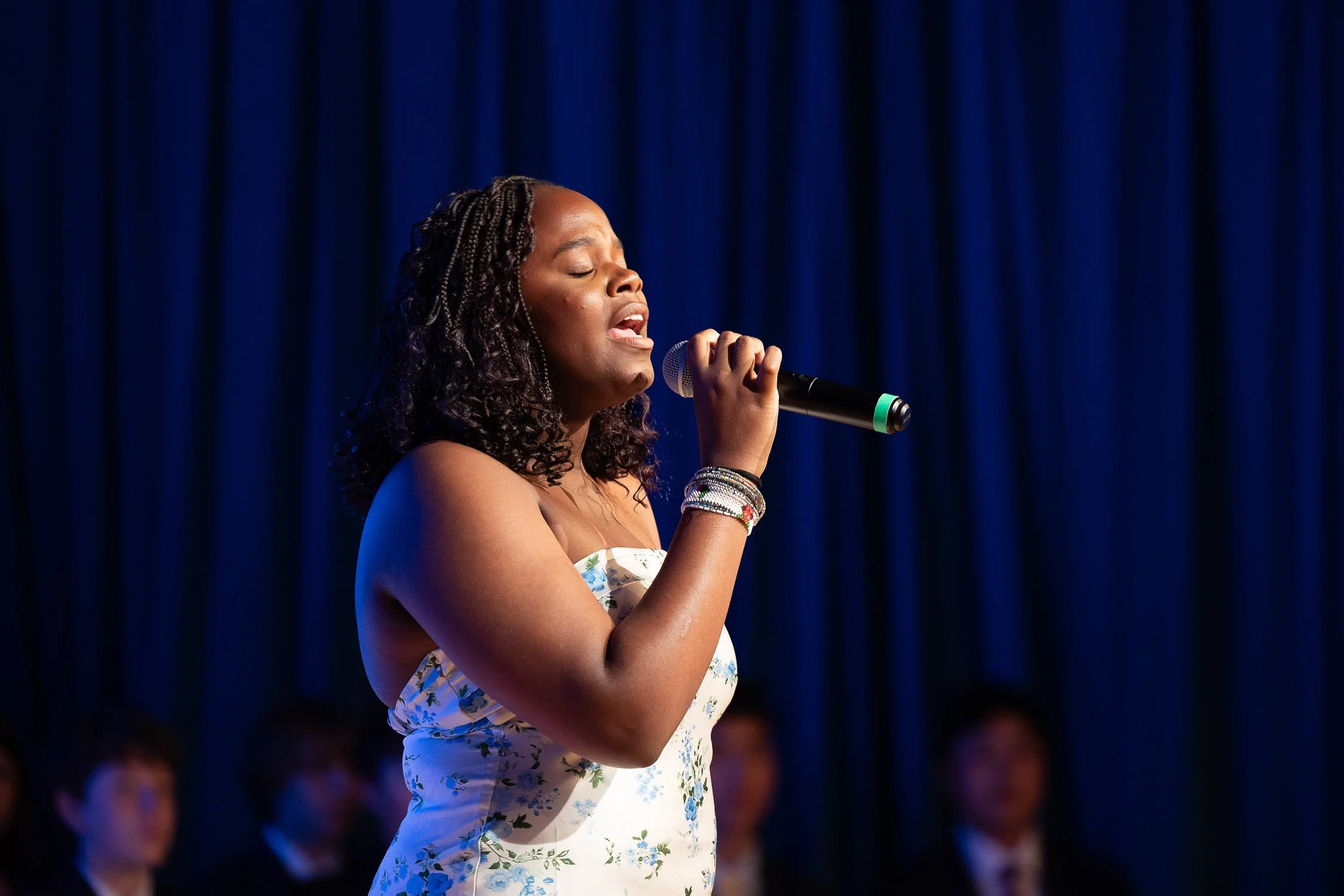 A middle school student singing into a microphone on stage during private school graduation ceremony.