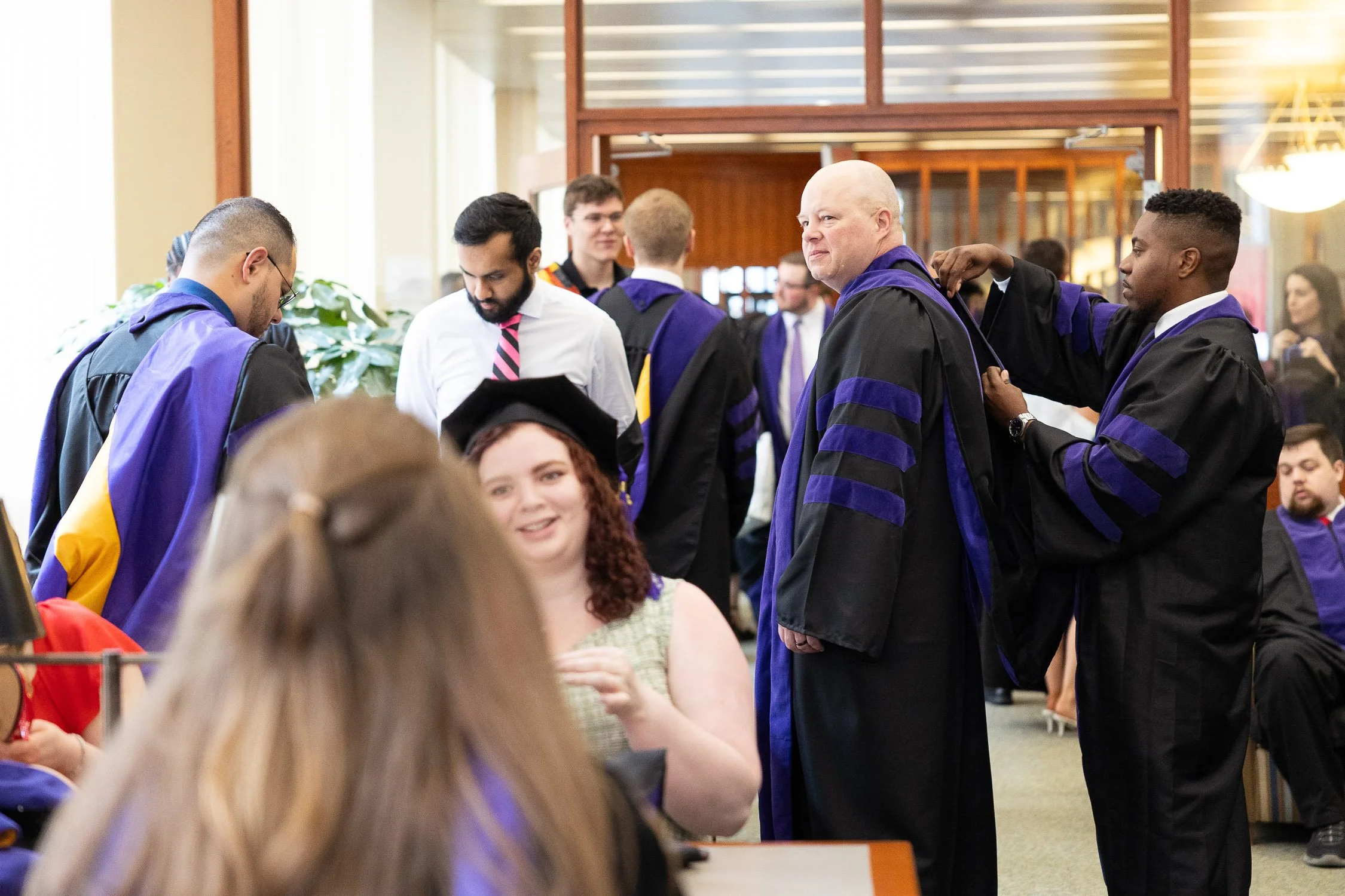 Law school graduates in caps and gowns preparing for a ceremony in library.