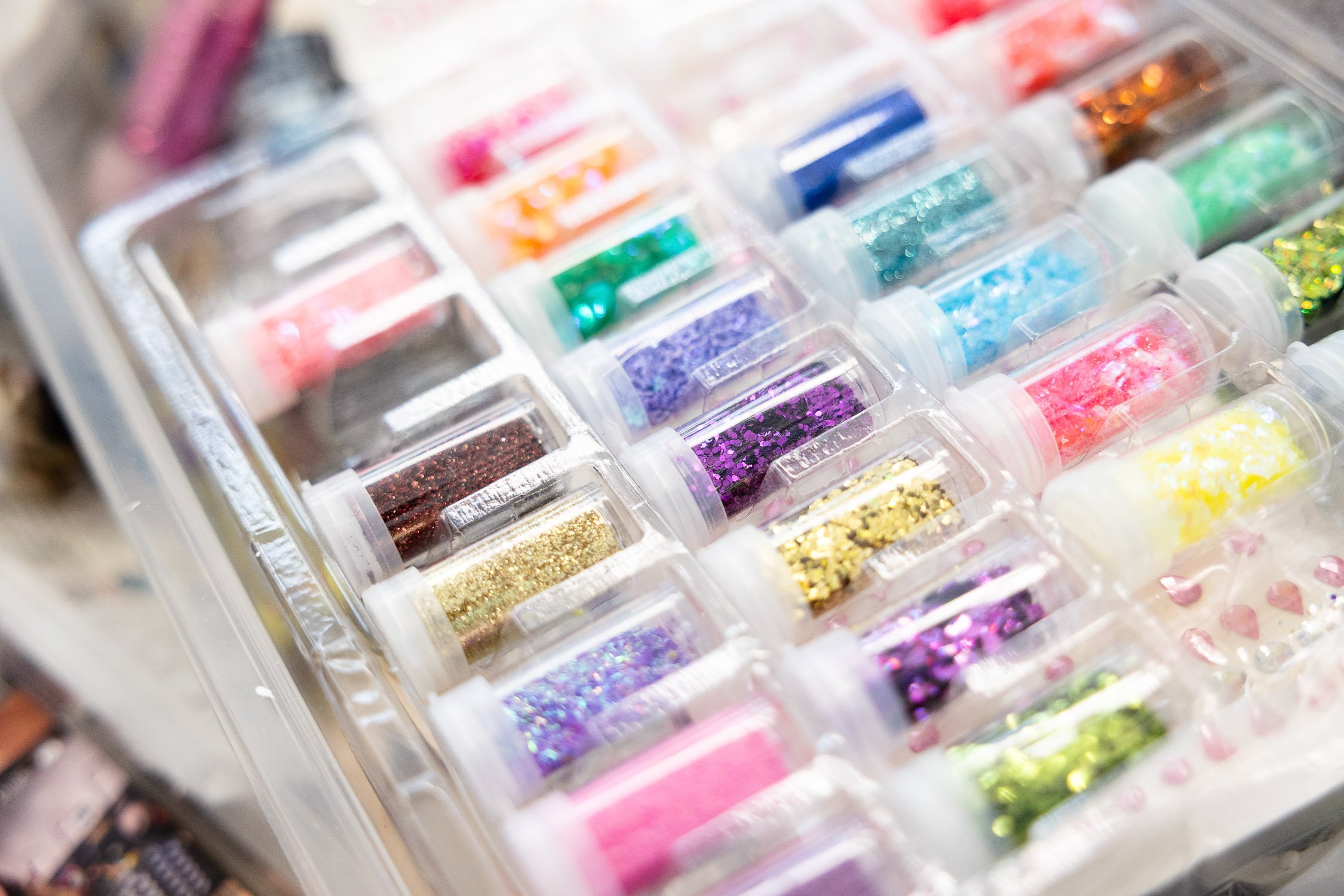 A plastic organizer box containing small containers filled with colorful glitter for crafting.