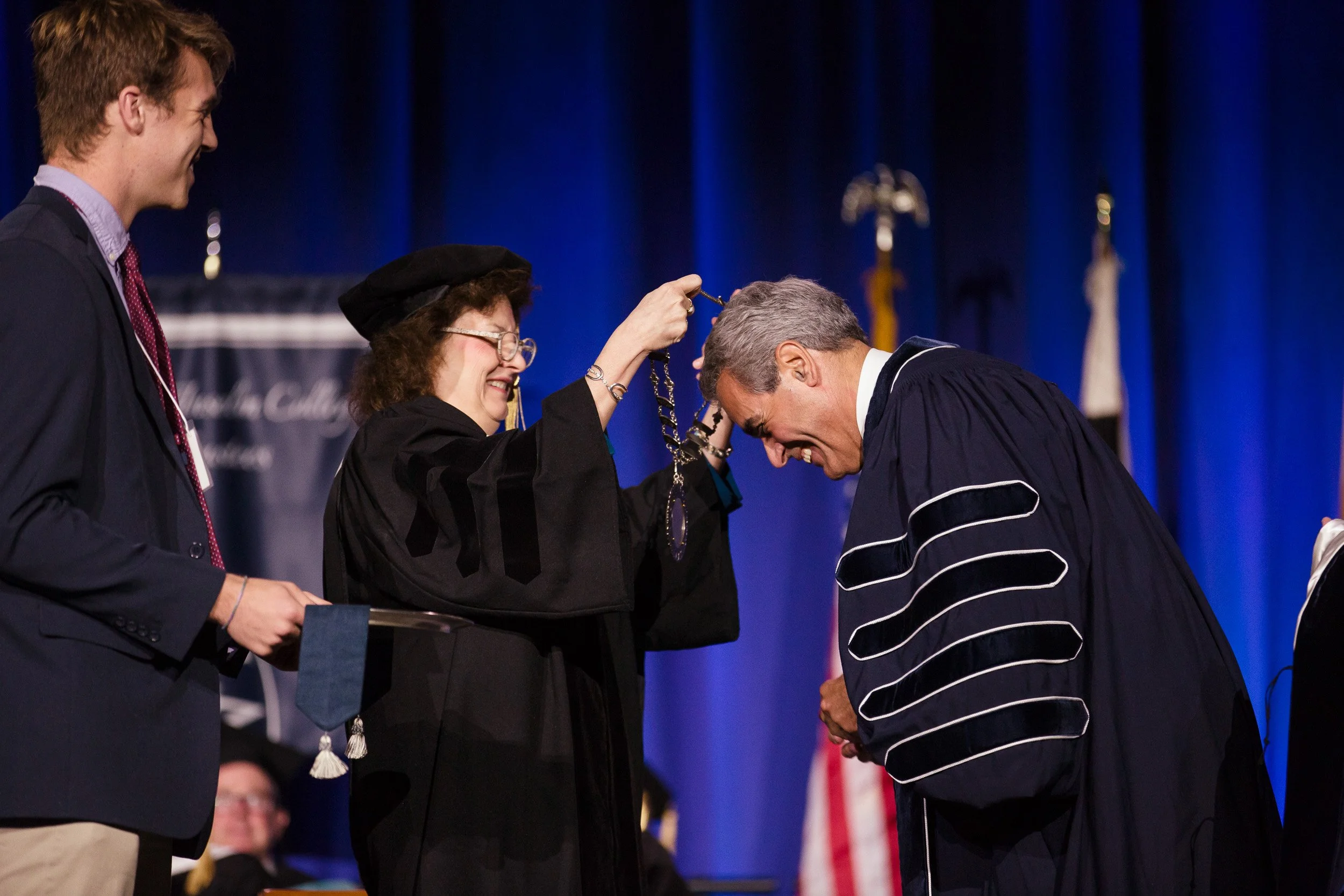 A woman in academic regalia placing a medal on a man during a graduation ceremony.