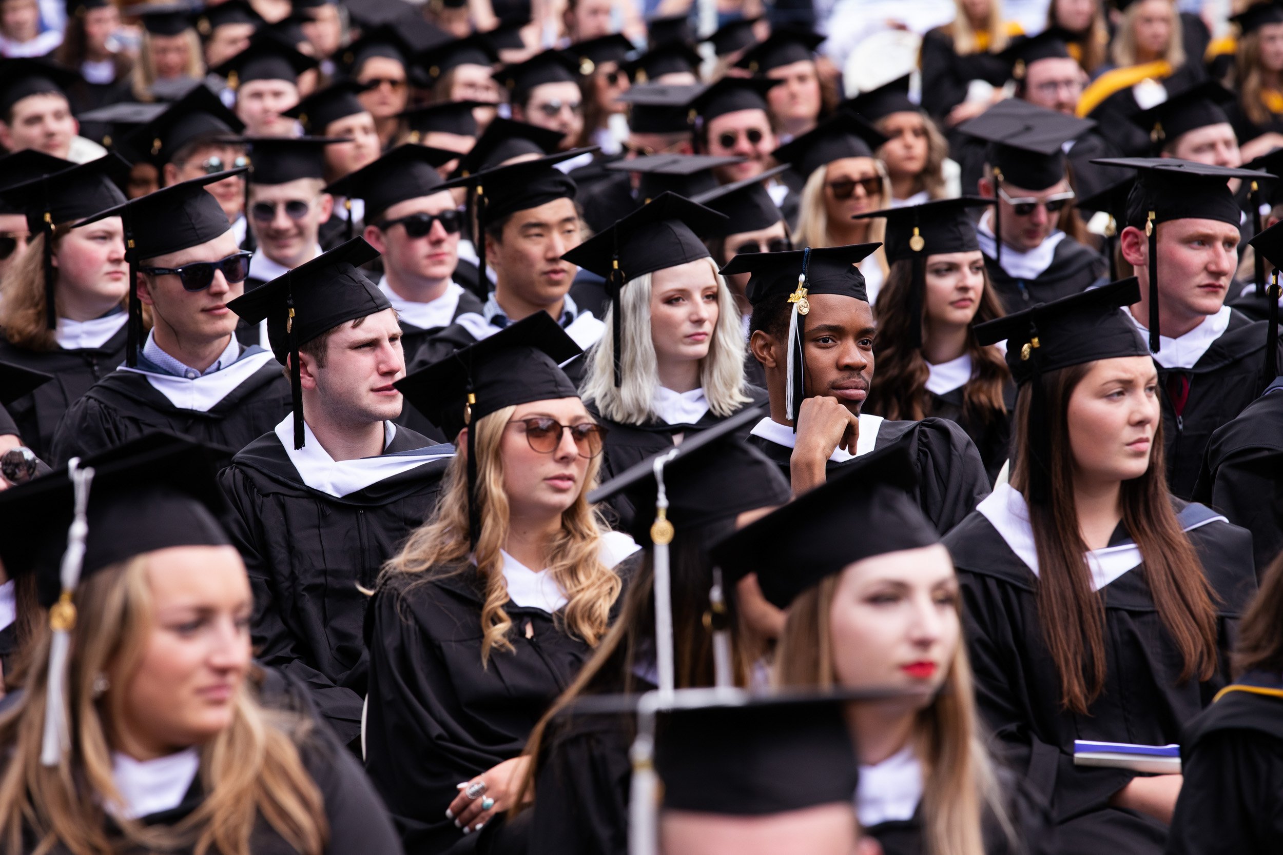 A large group of students dressed in black graduation caps and gowns attending a graduation ceremony at Saint Anselm College.