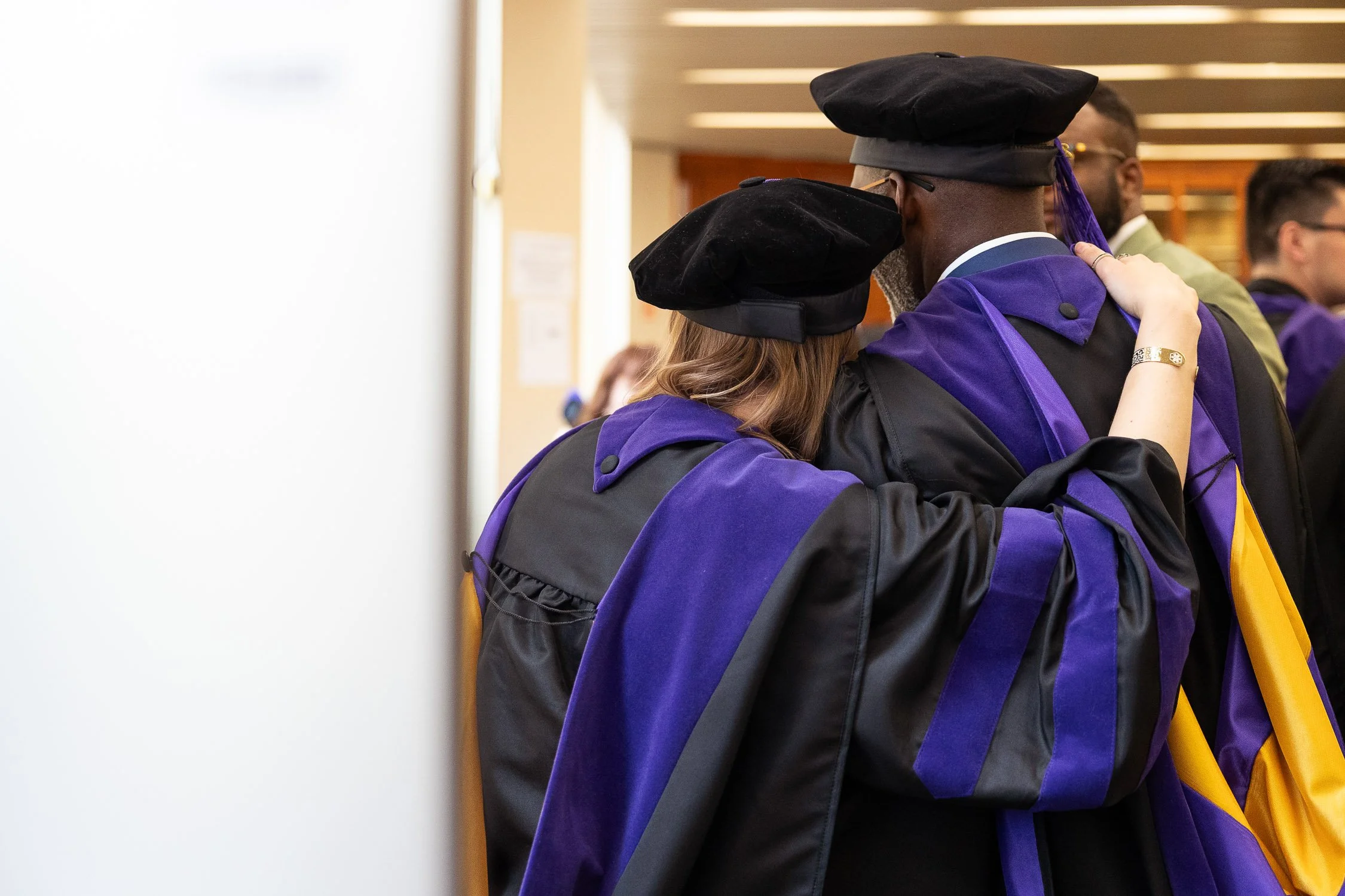 Graduates in academic regalia hugging before a graduation ceremony.