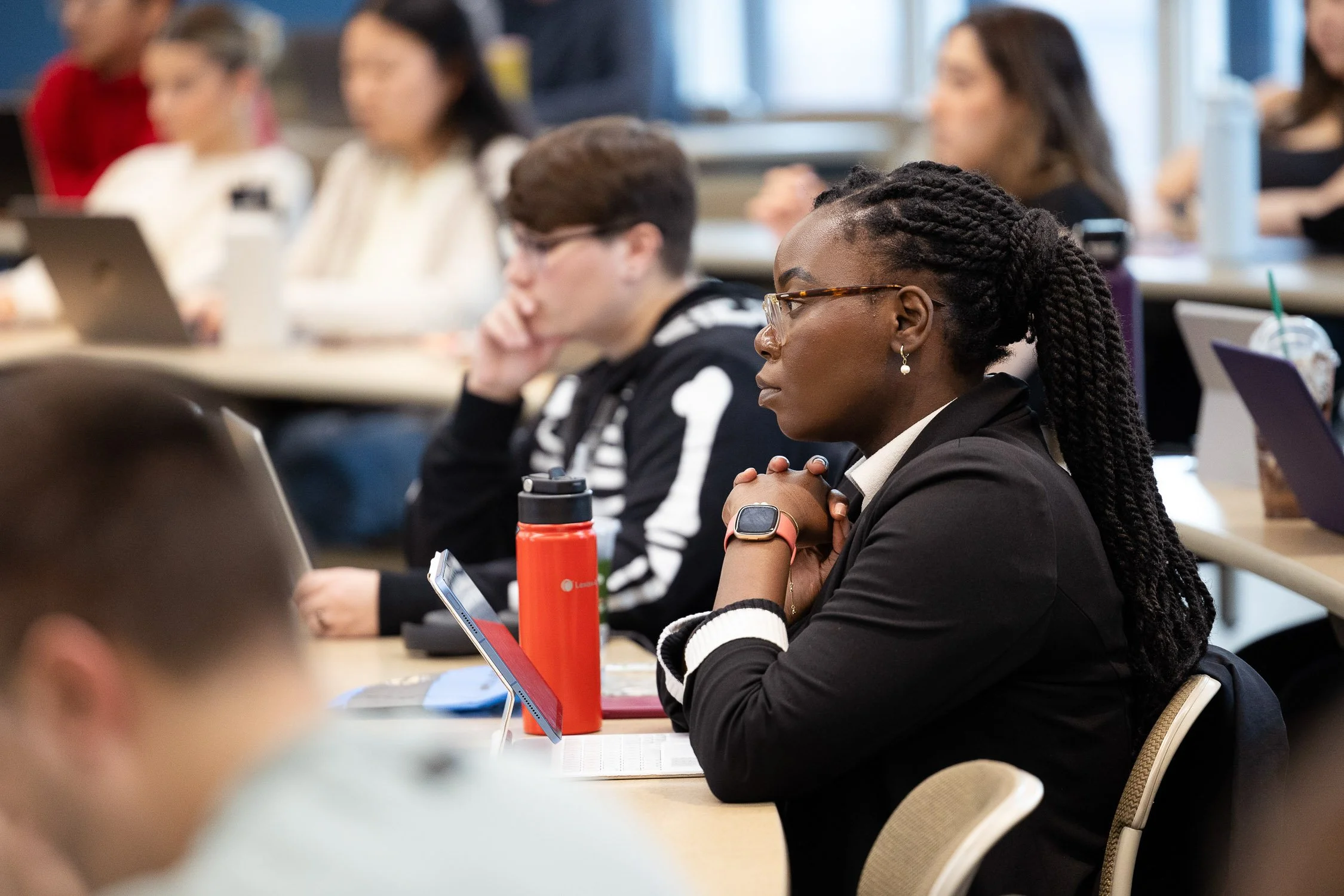 Law students attending a lecturer, sitting with laptops and notebooks, listening attentively.