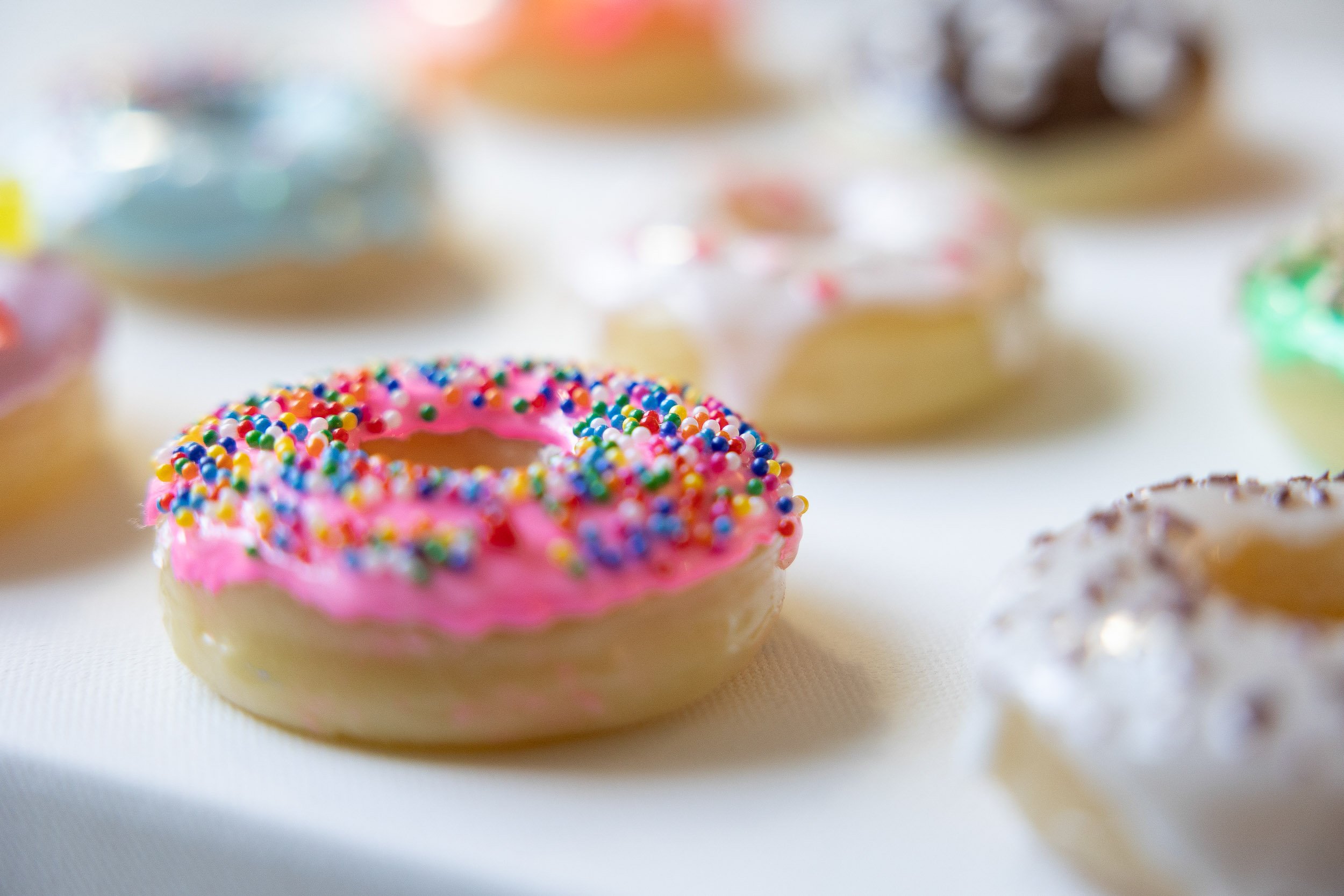 Close-up of a pink frosted resin donut with colorful sprinkles, surrounded by other assorted donuts.