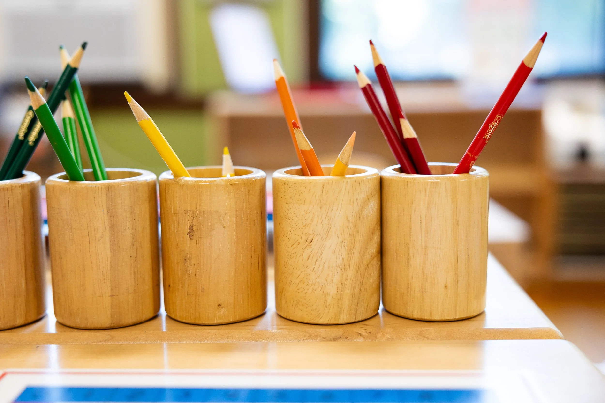 Colorful colored pencils in wooden cups on a classroom table.