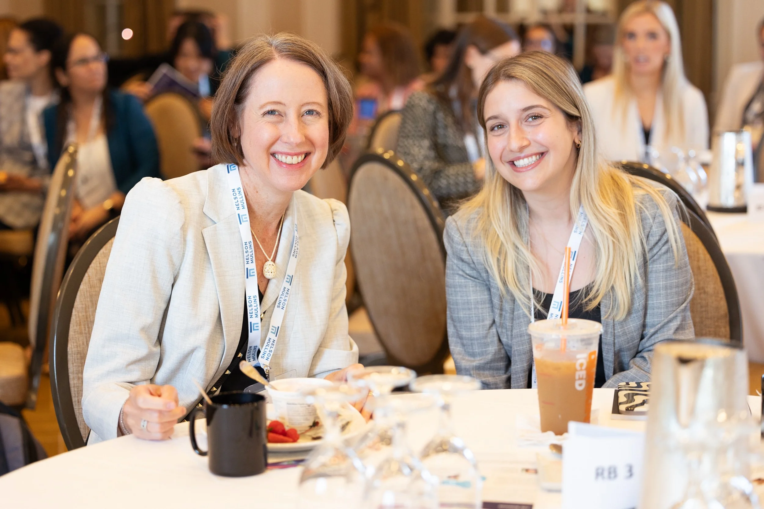 Two women smiling and sitting at a table during a law conference in Boston.