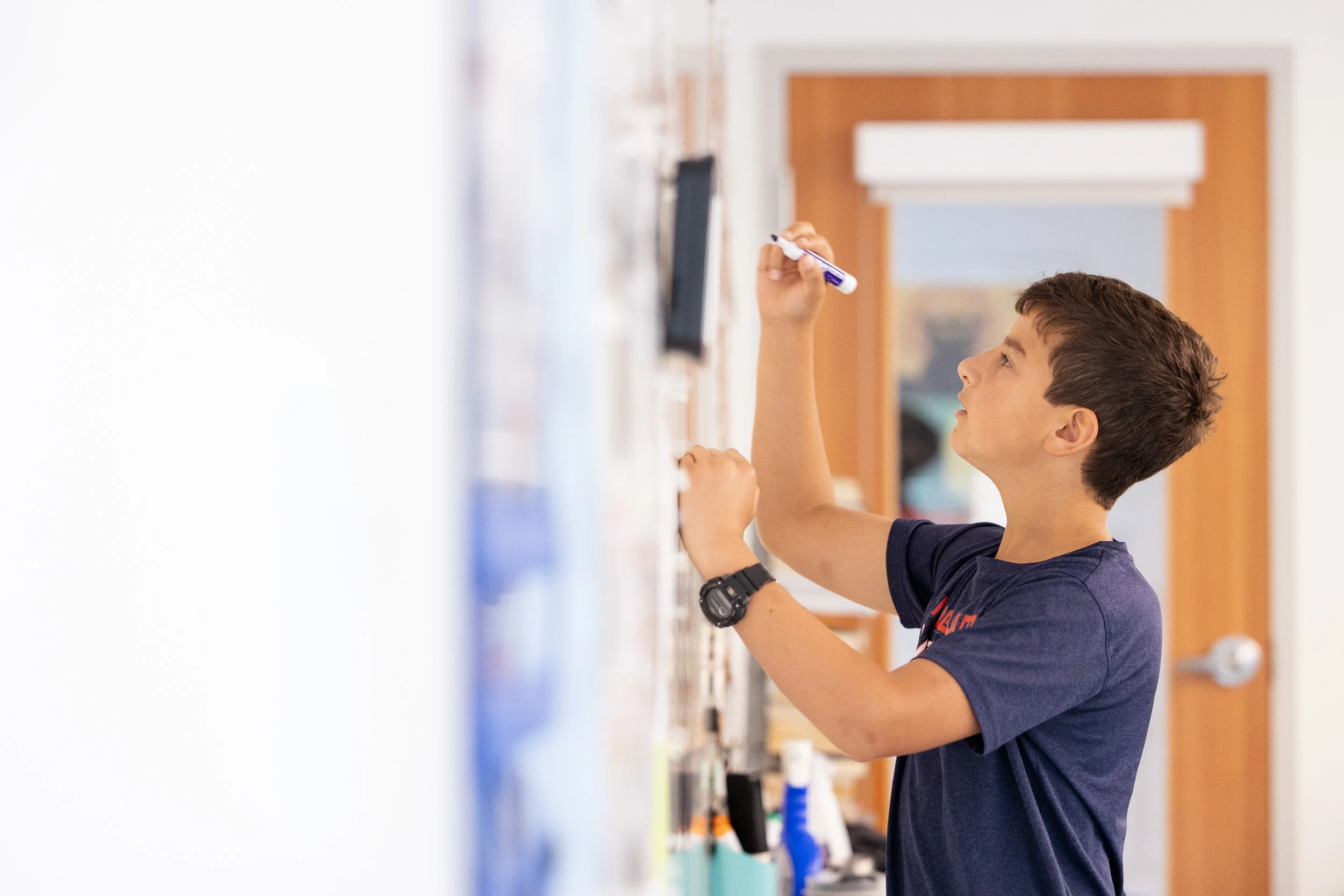 A boy writing on a whiteboard in a classroom.