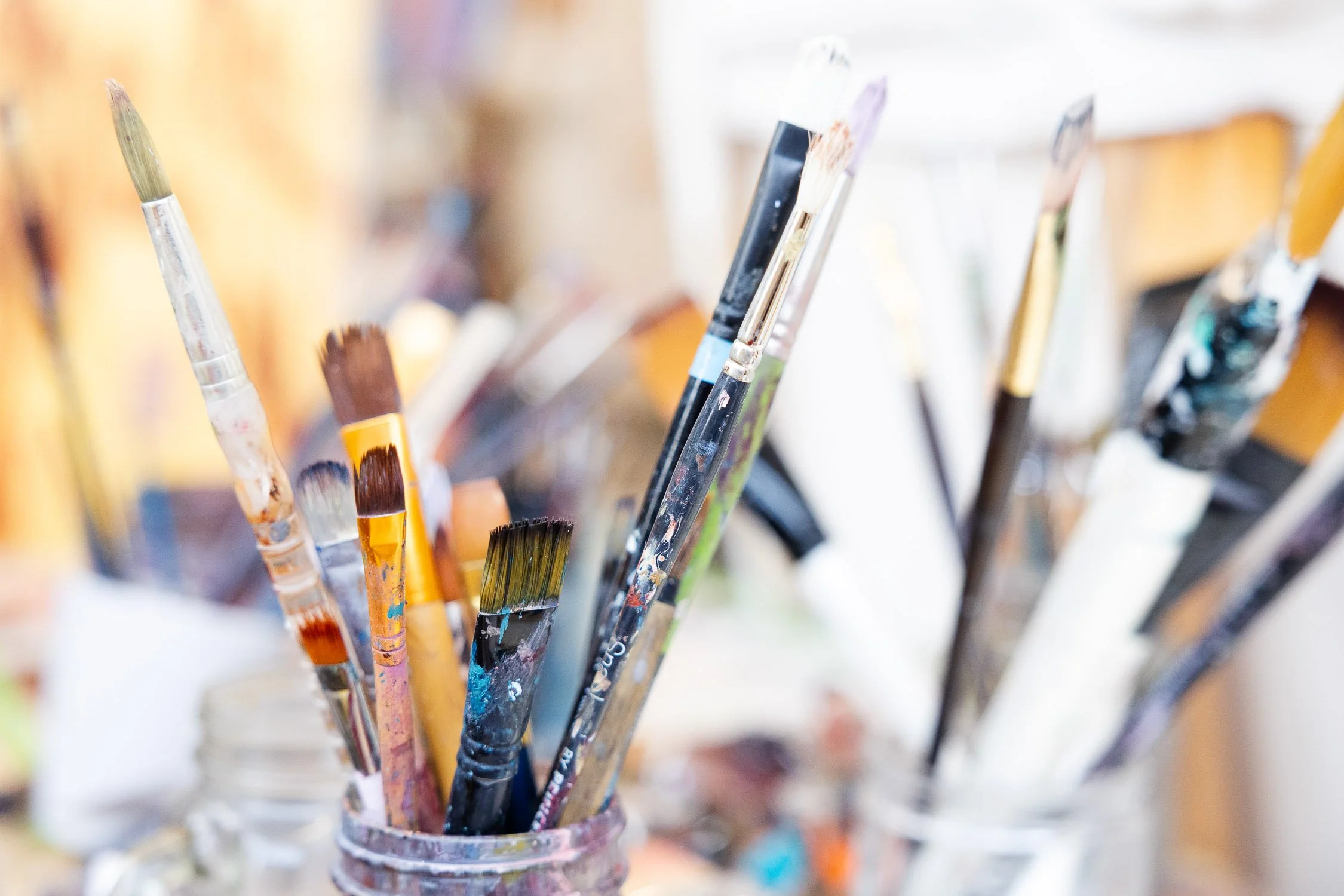 Close-up photo of various paintbrushes in a glass jar with paint stains on the brushes.
