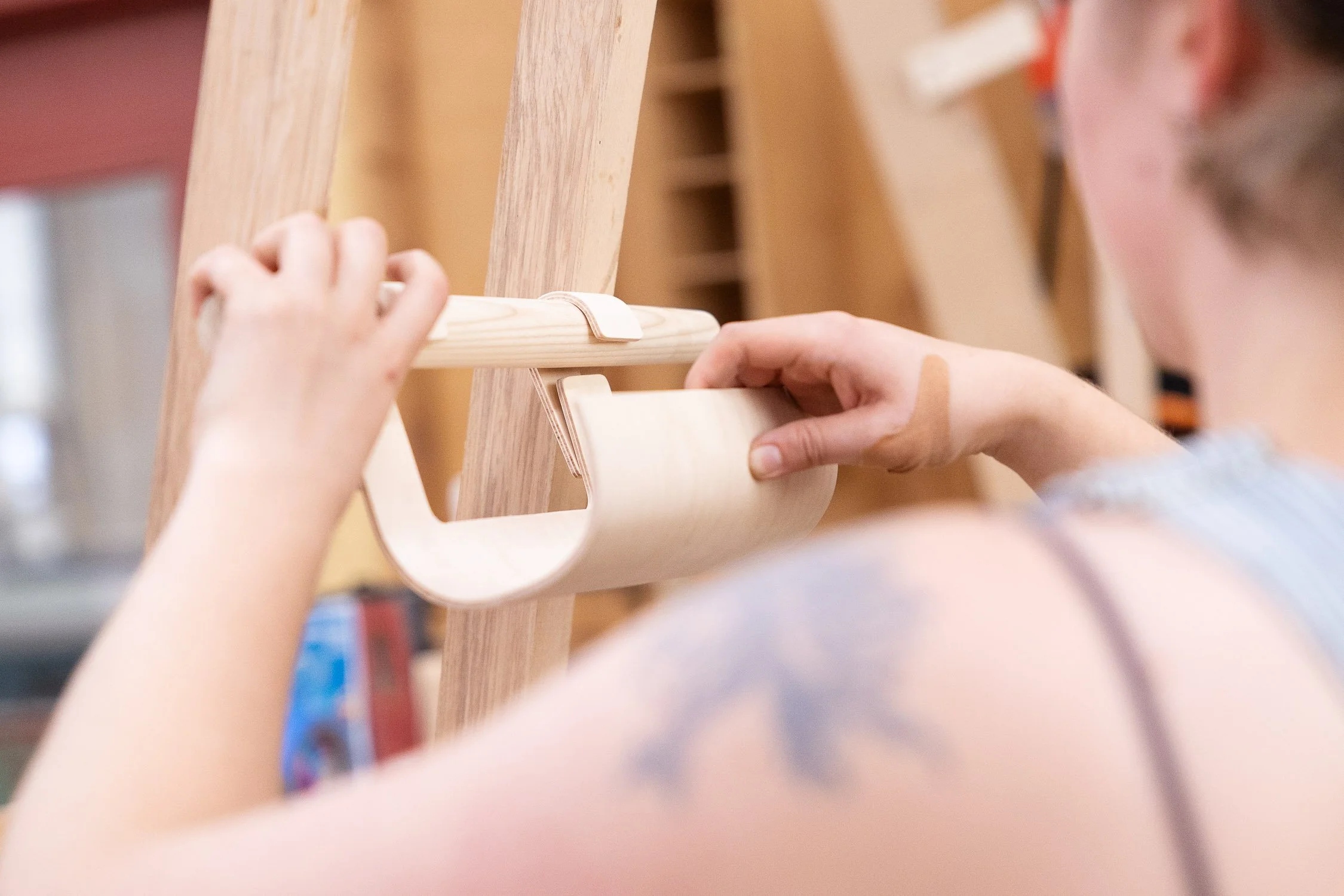 A student working on a woodworking project, holding a wooden strip and positioning it on a larger wooden structure.