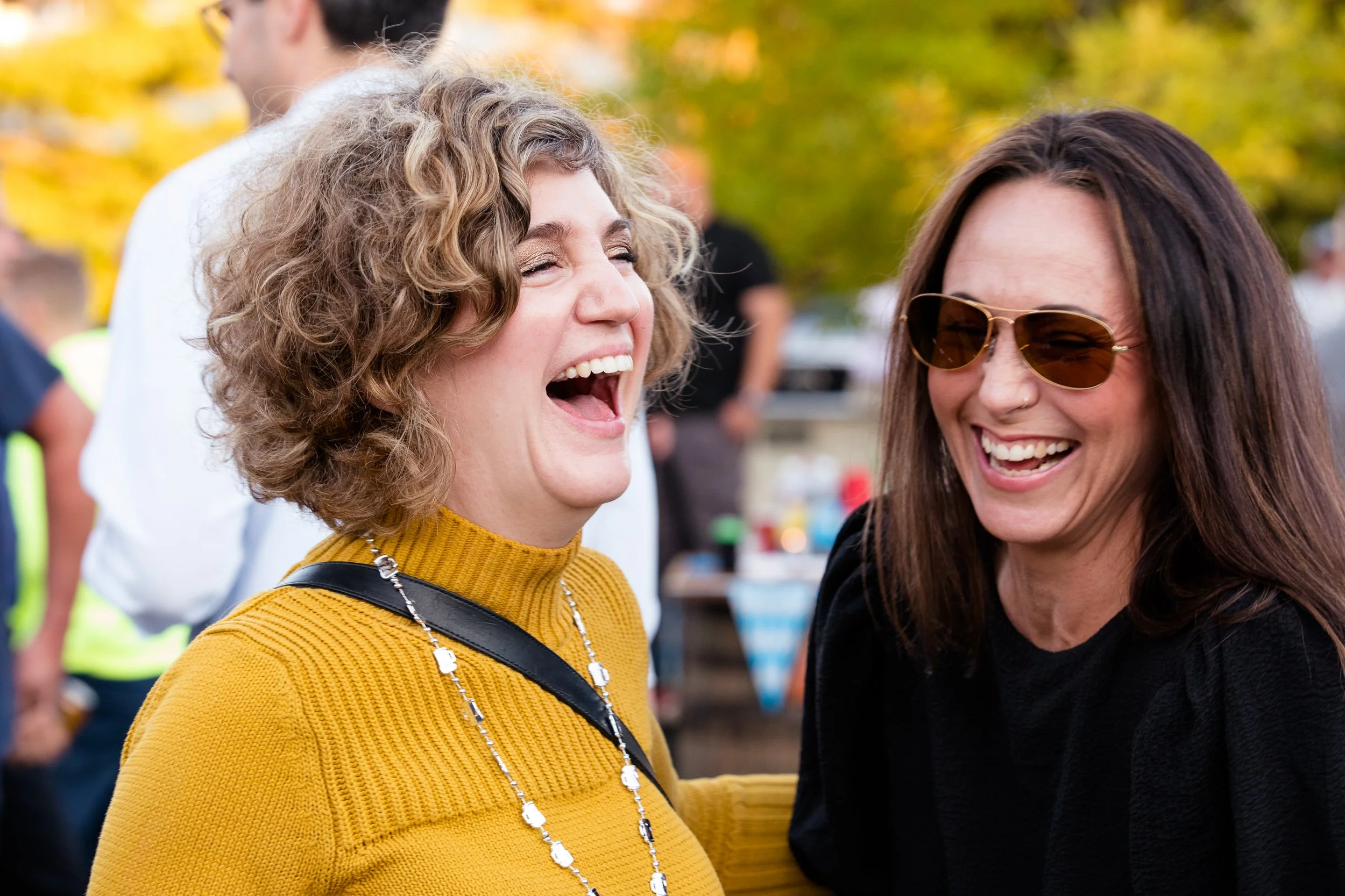 Two women are smiling and laughing together outdoors at an Oktoberfest event in Boston.