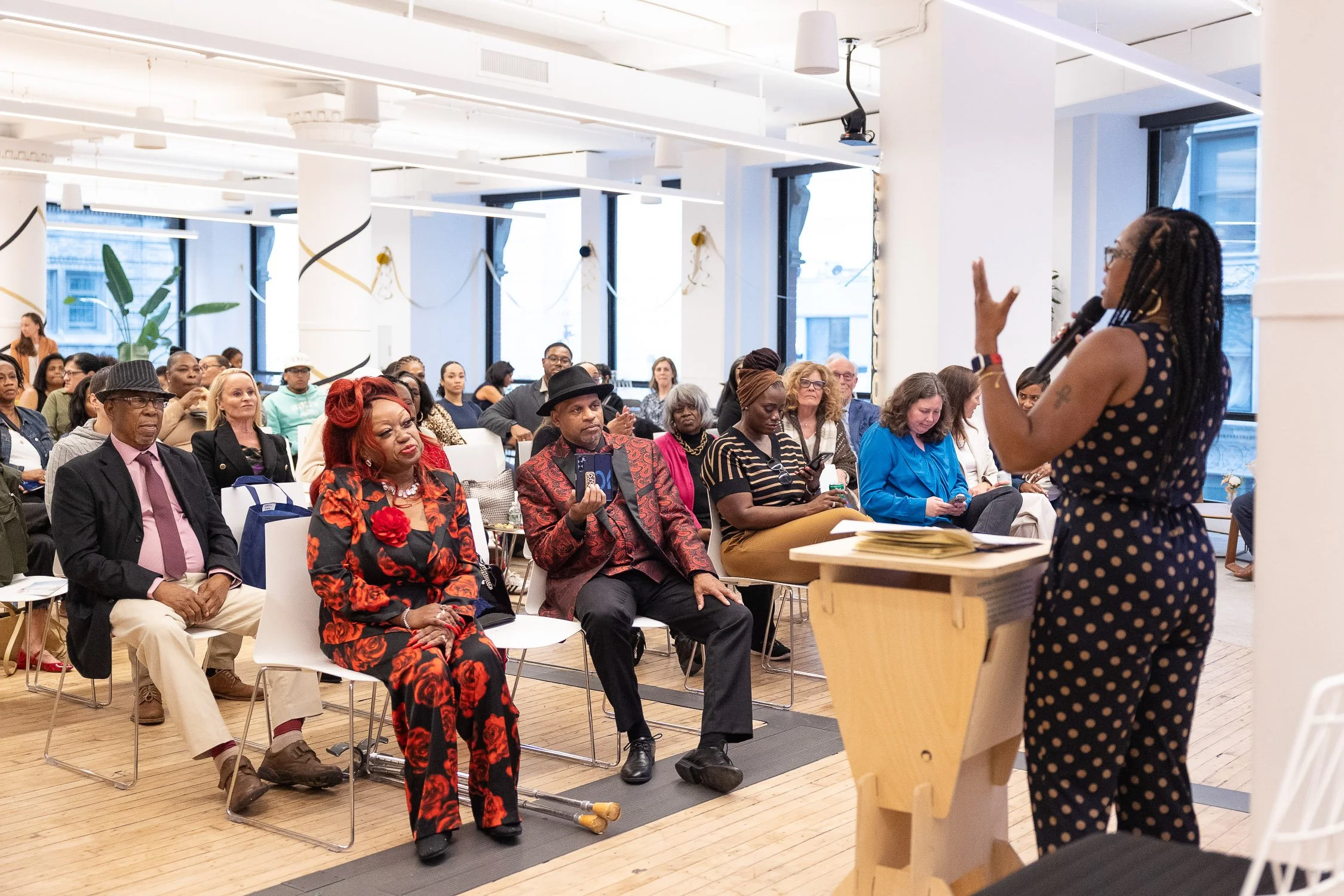 A woman speaking into a microphone, addressing an audience in a bright, modern room at Sasaki Foundation in Boston.