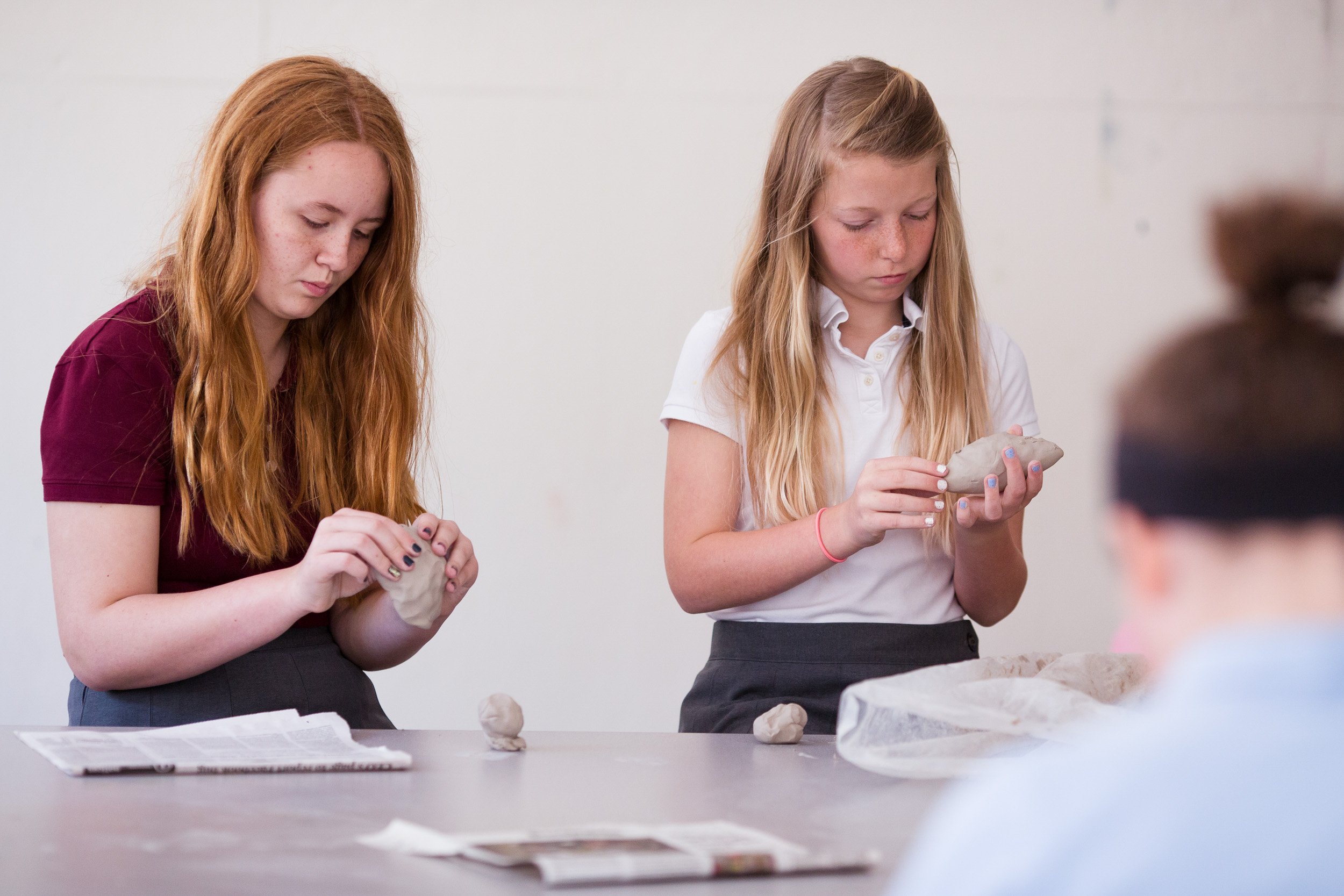 Two middle school students working with clay at a table in a classroom setting.