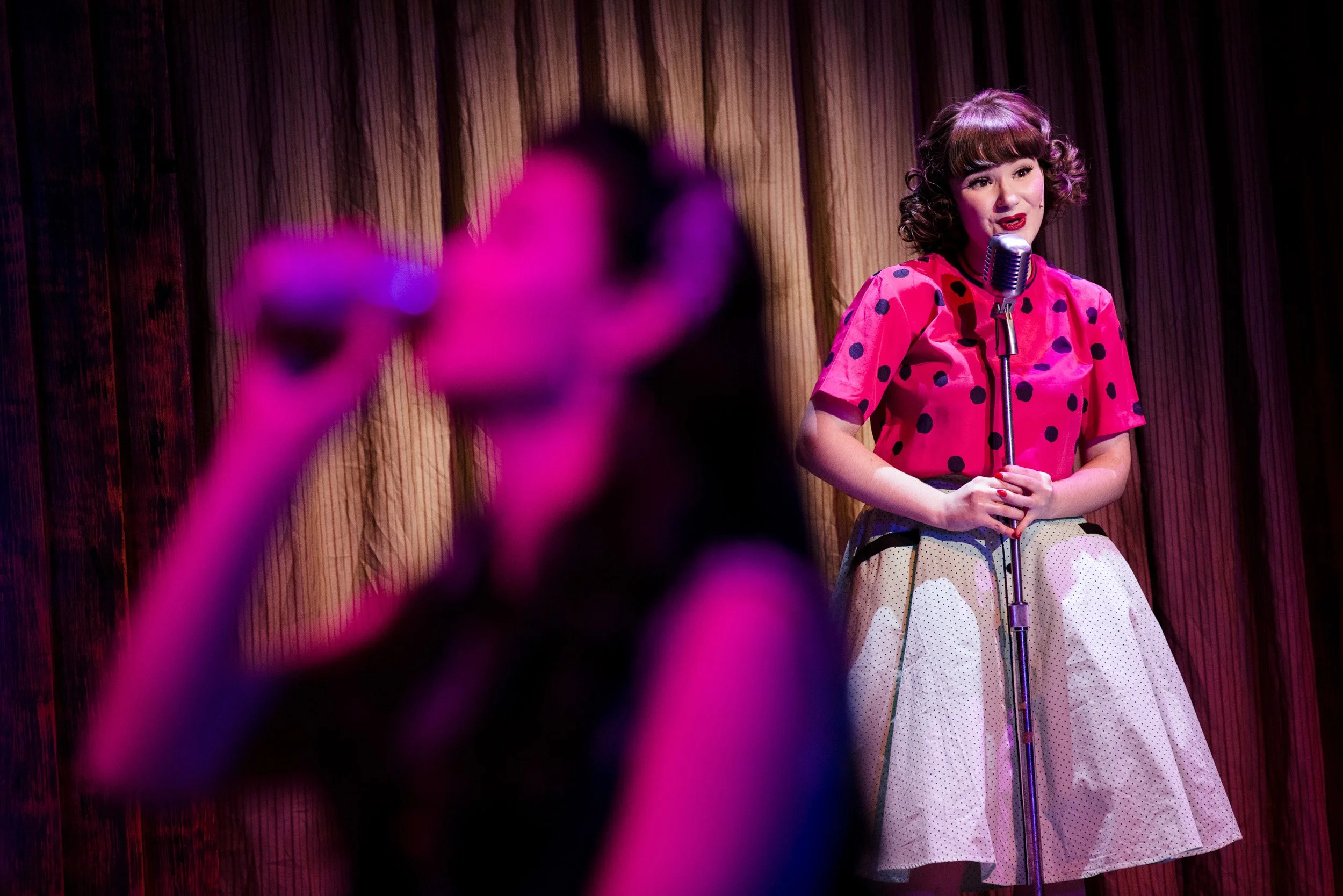A high school actor standing on stage in front of a microphone, performing in a musical production at an independent school in Massachusetts.