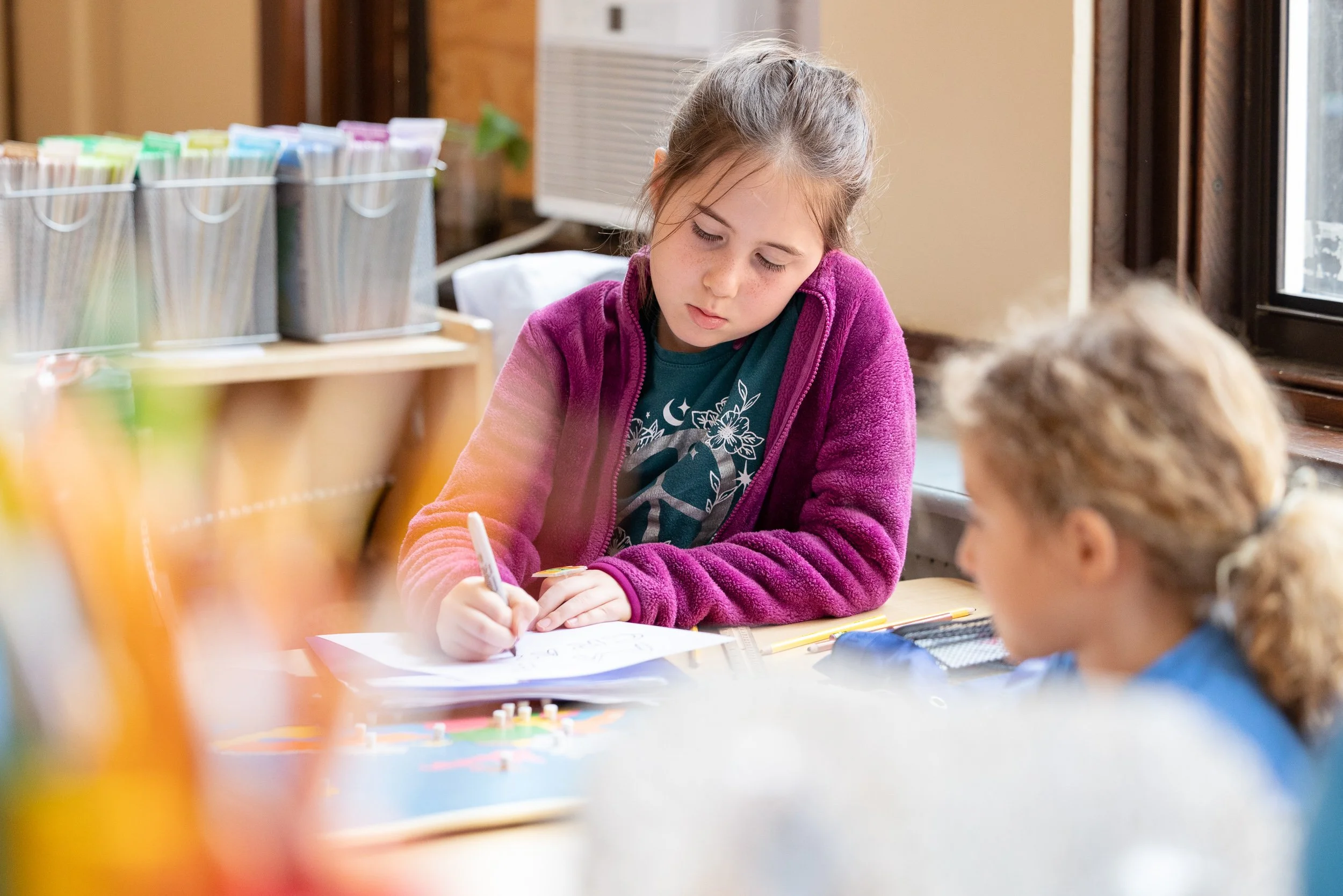 Two elementary students sitting at a table in a Boston Montessori classroom.