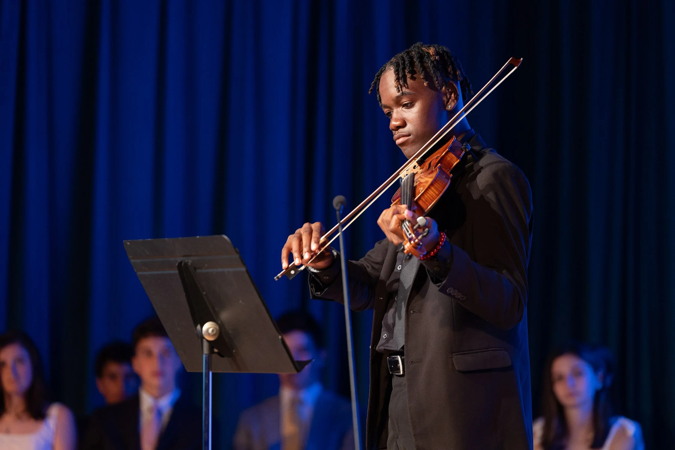 A middle school student playing the violin during a performance on stage during an independent school graduation ceremony.