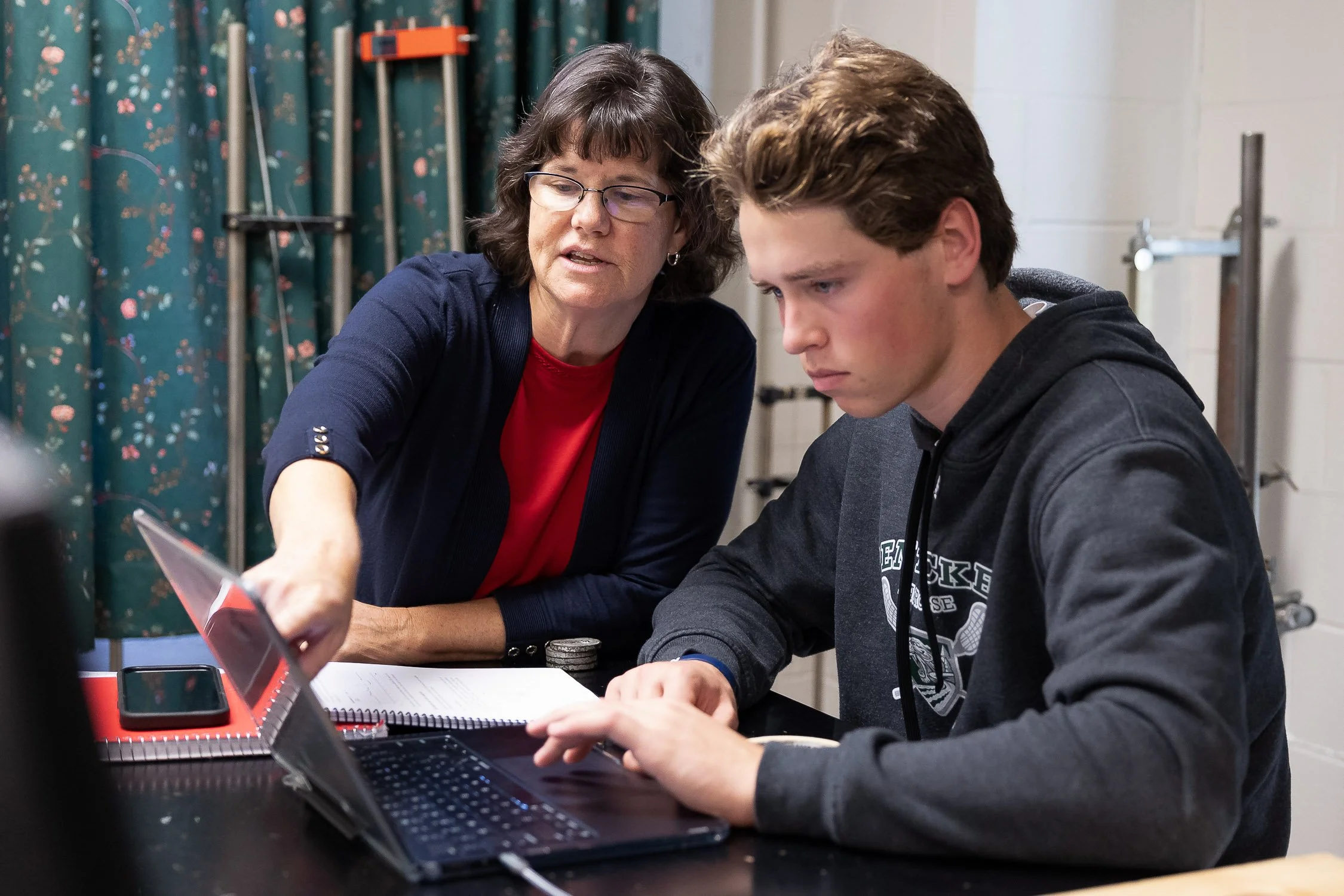 A college physics professor with glasses explaining something to a young student on a university campus in New Hampshire. 